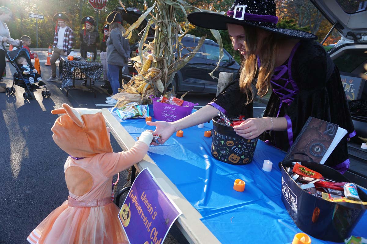 A Penn State Hazleton student dressed in a witch's costume hands candy to a young child dressed as Bingo from Bluey. 