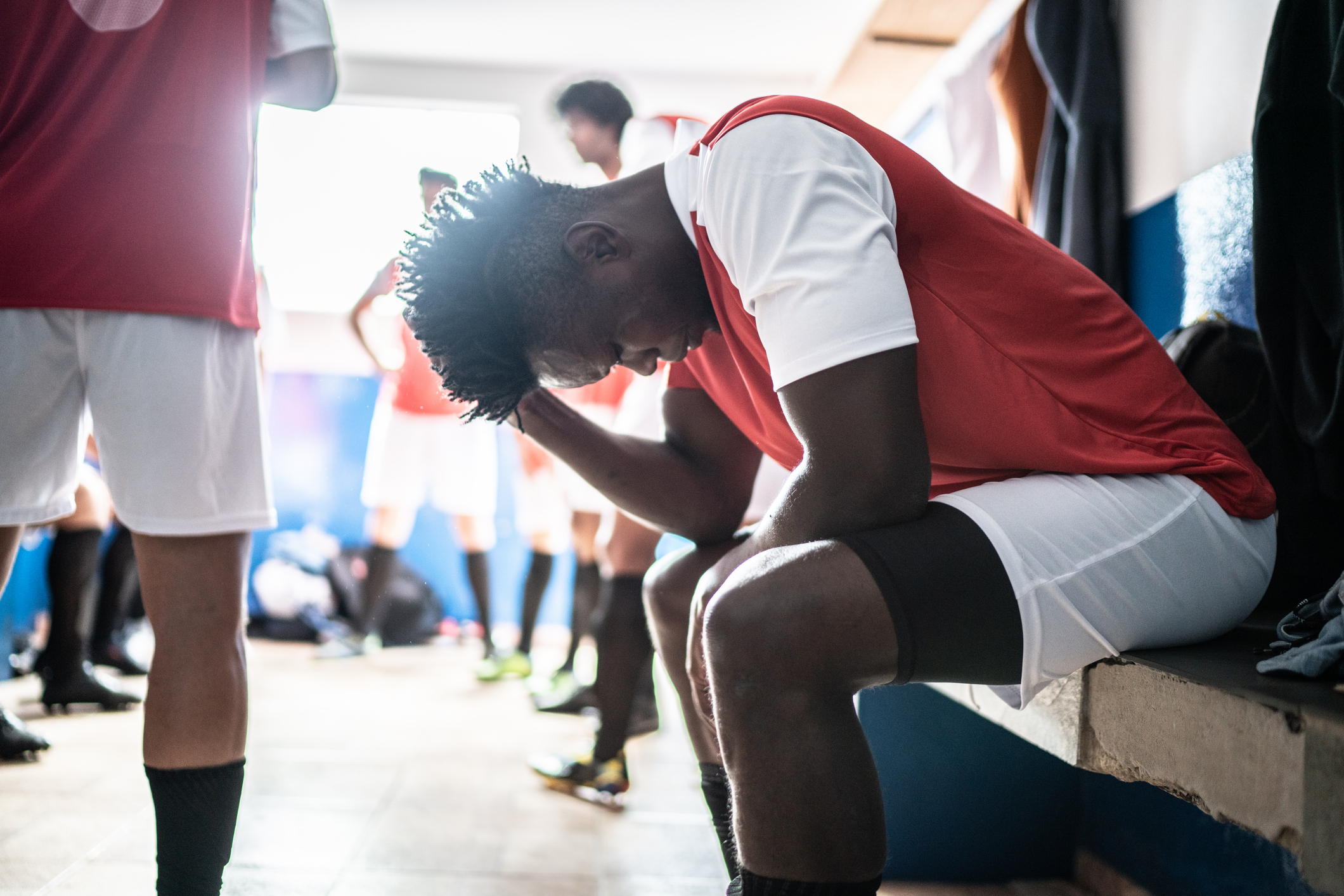 Male athlete in locker room holds his head and looks pained