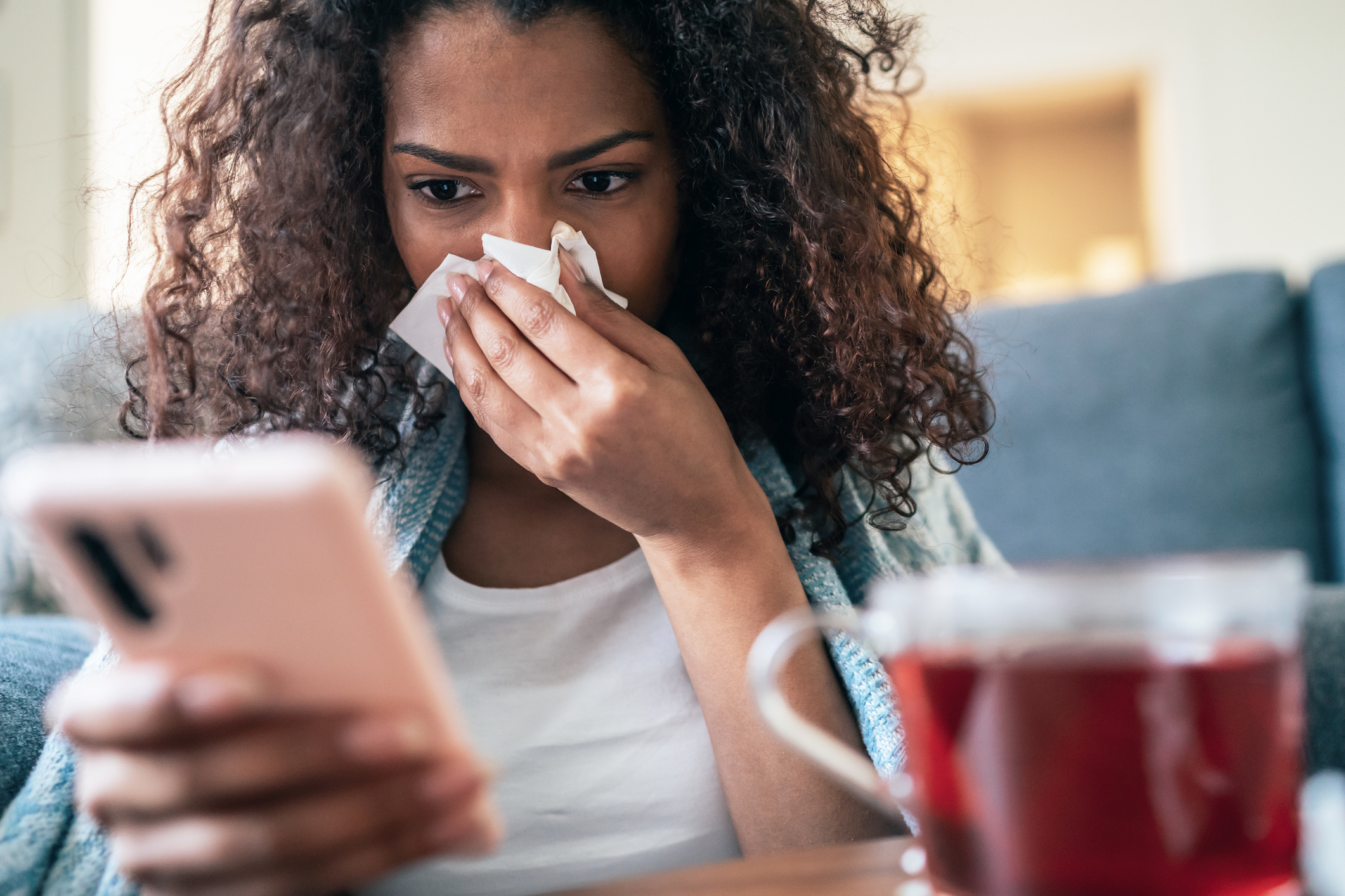 A person using their smartphone while blowing their nose with a tissue