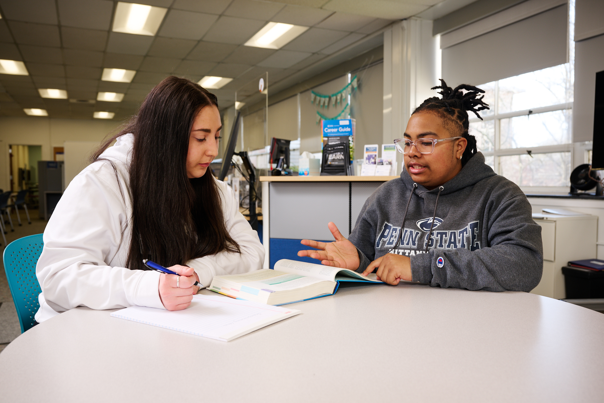 A student learner and tutor sitting at a table looking at a book