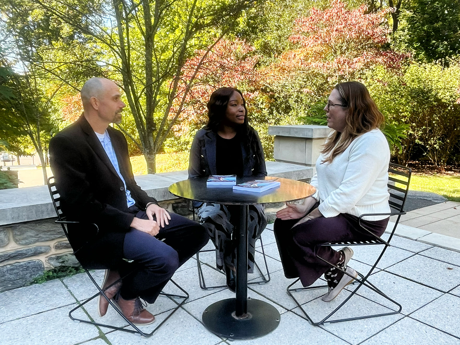 Three people around an outdoor table talking