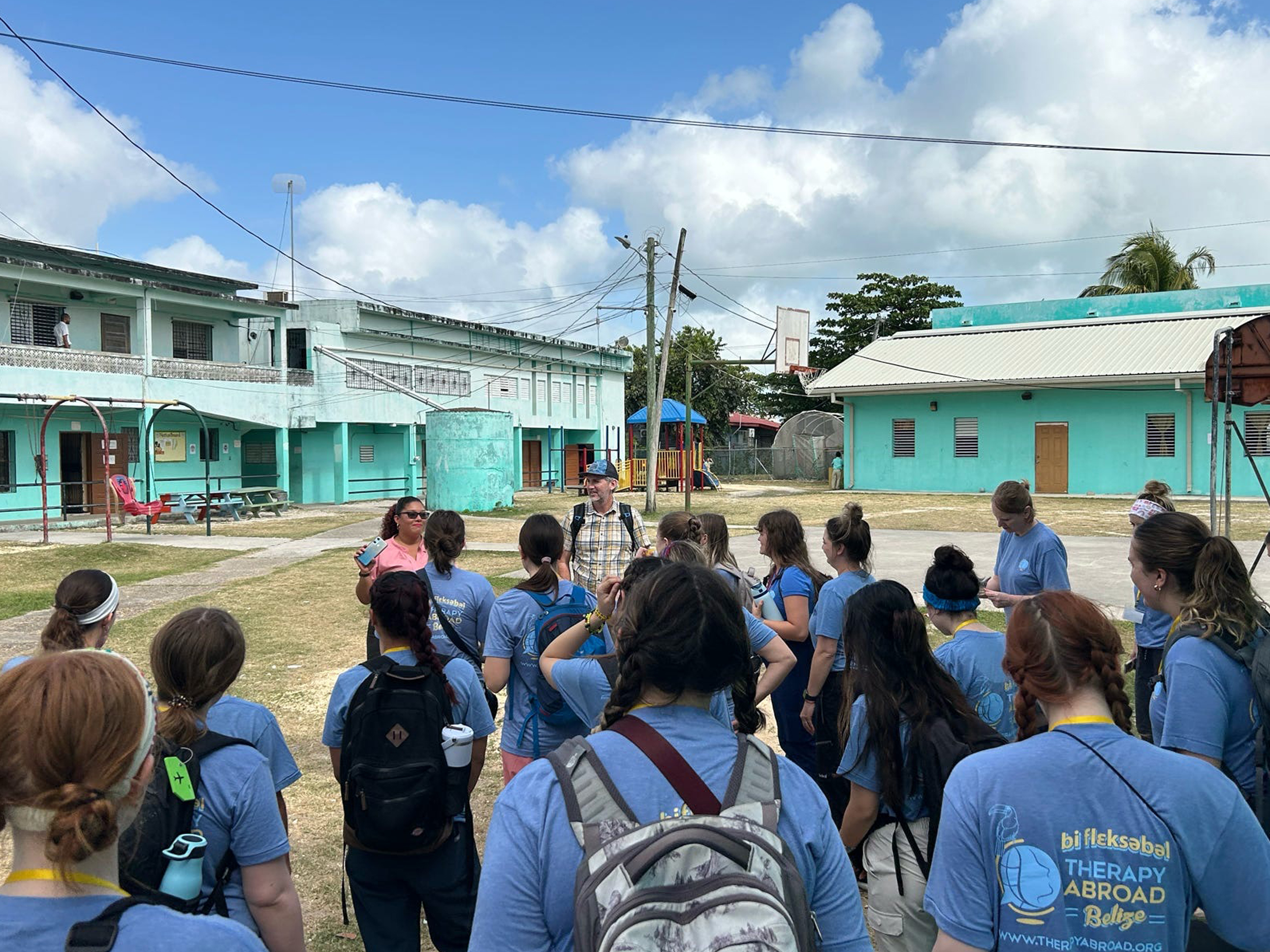 About 15 Penn State students stand in a courtyard of a school in Belize while trip leaders talk to them