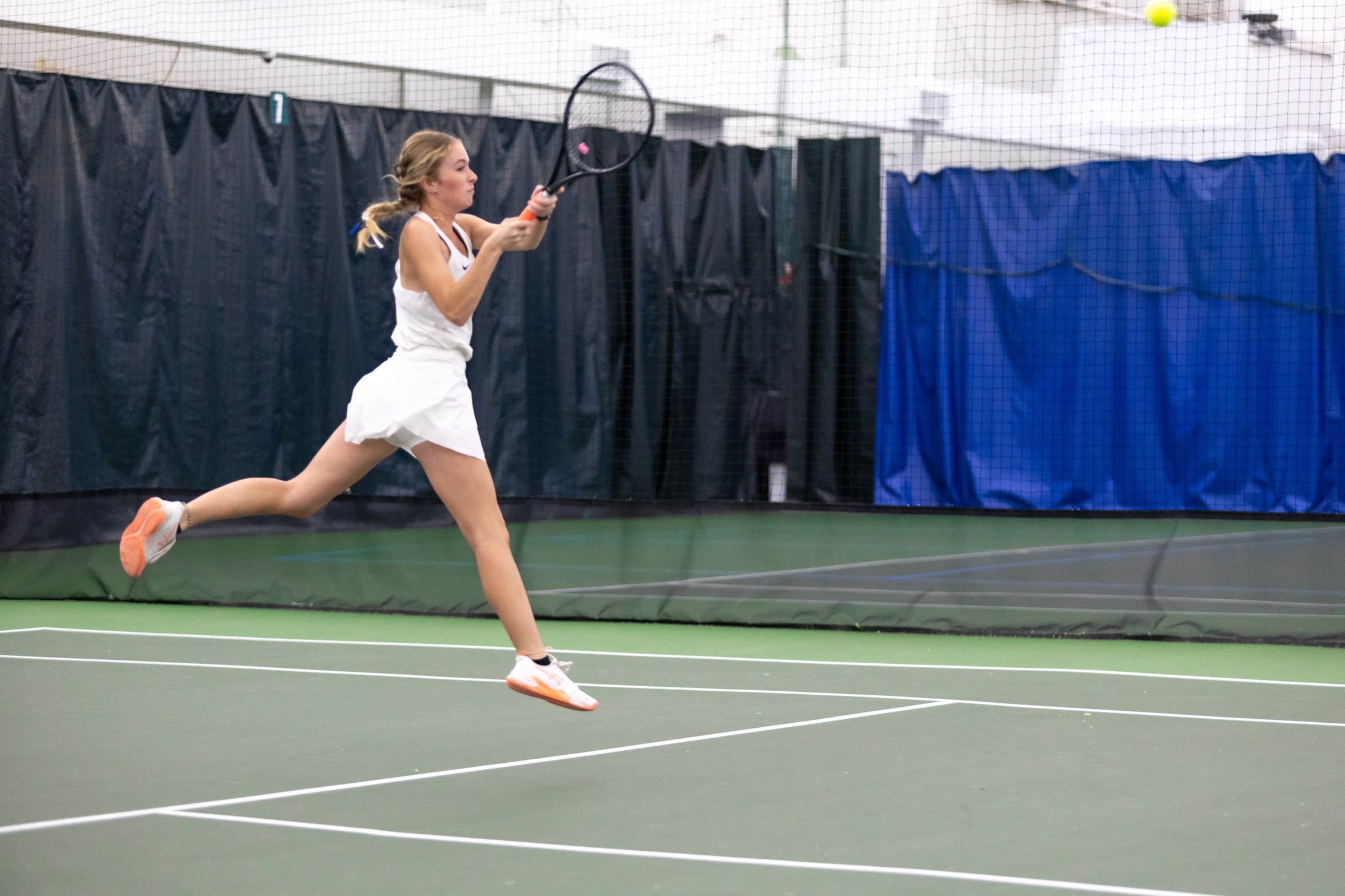 A Penn State Behrend tennis player jumps while hitting the ball.