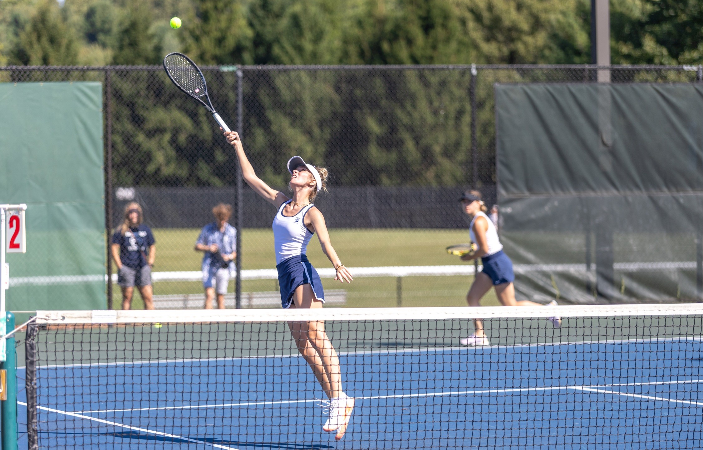 A member of the Penn State Behrend women's tennis team reaches up to hit a ball.