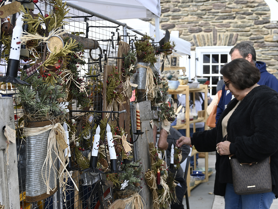 Two people at right look at holiday merchandise displayed at an outdoor booth.