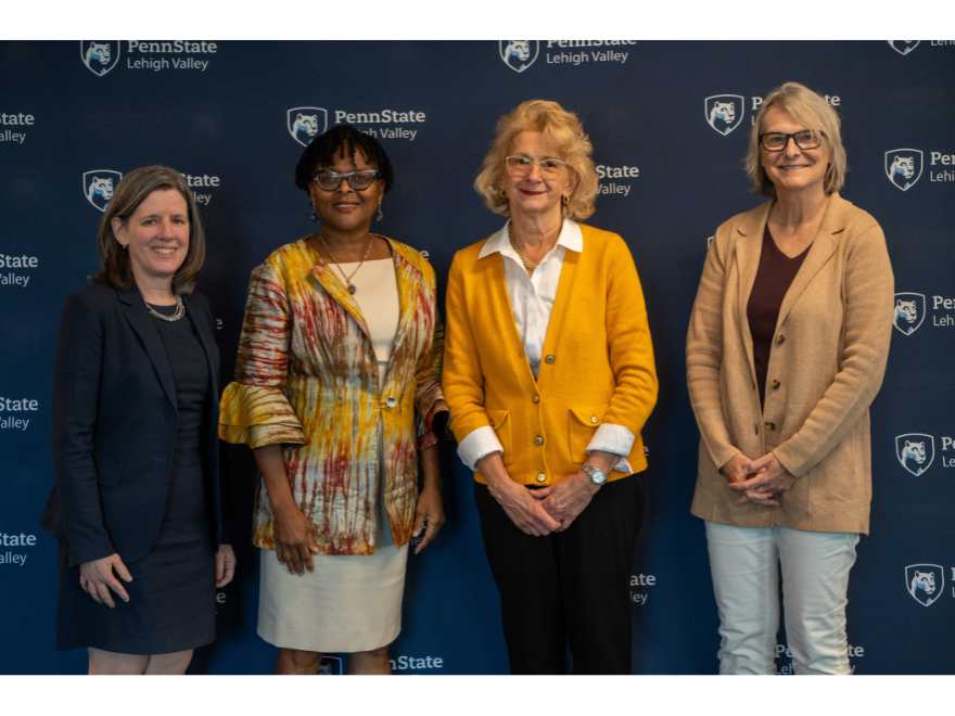 four women smile in front of a penn state step and repeat backdrop