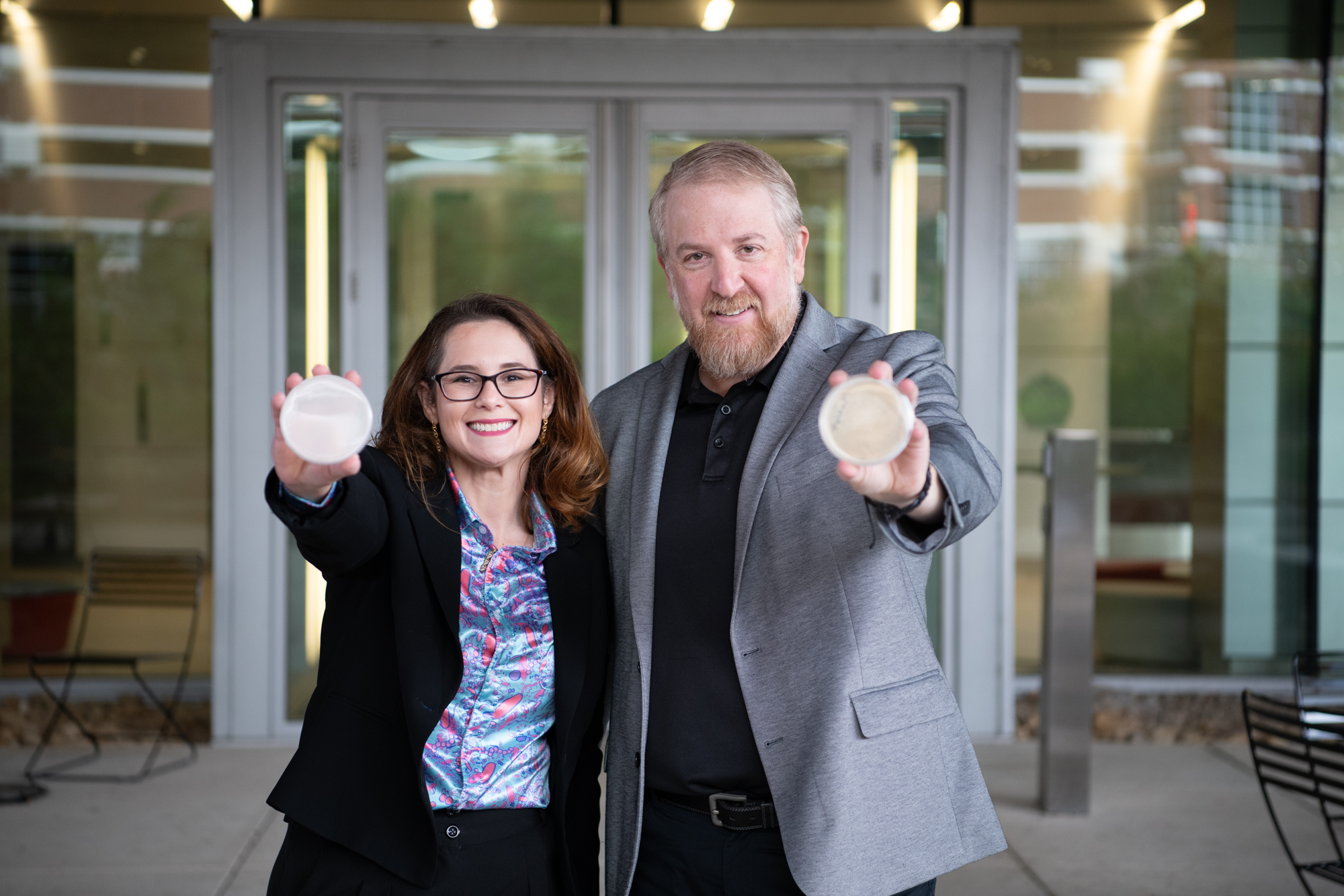 Image of two faculty members holding microbiome plates in front of the Millennium Science Complex