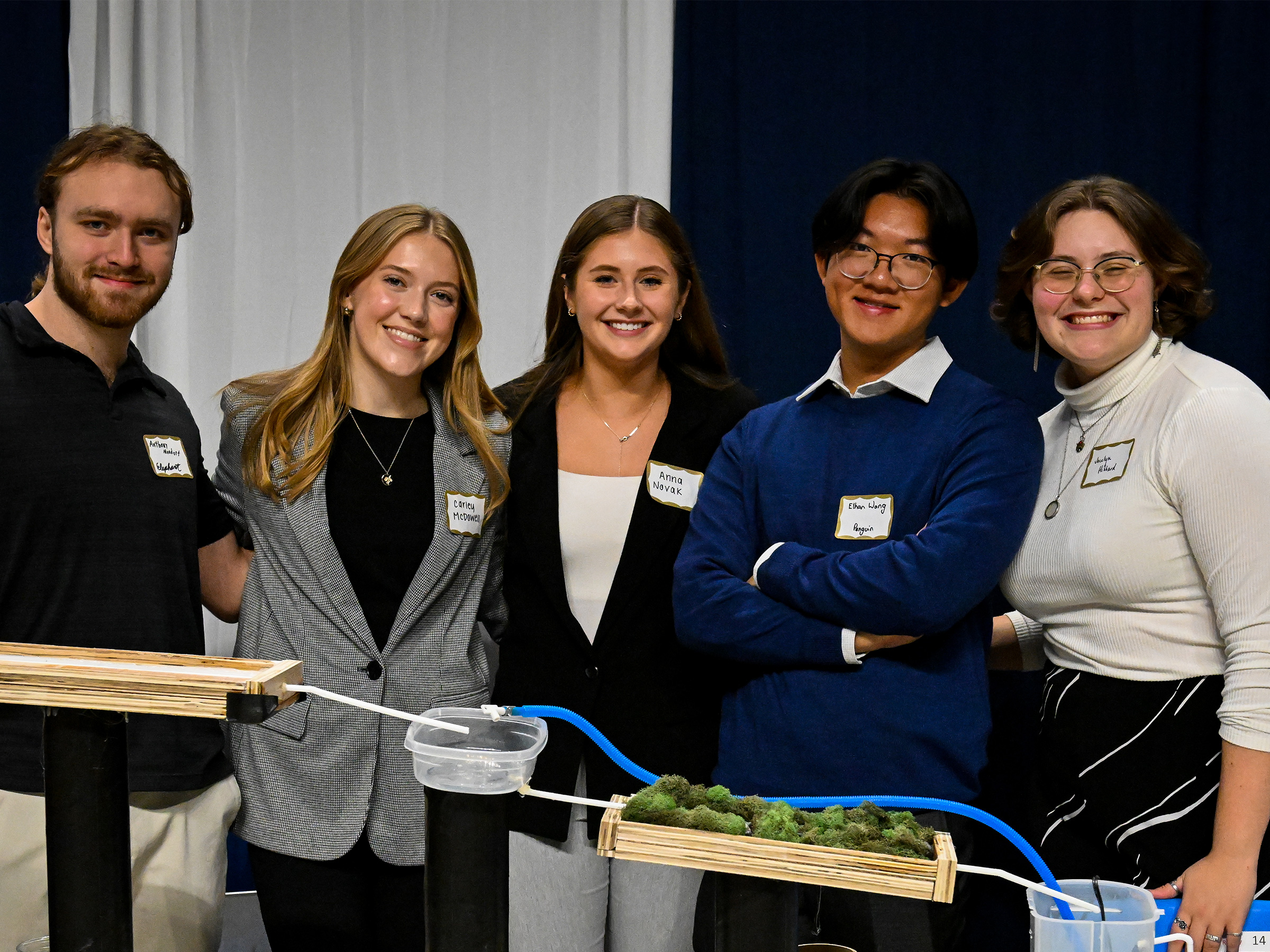 Students pose with an engineering project in a large event venue. 