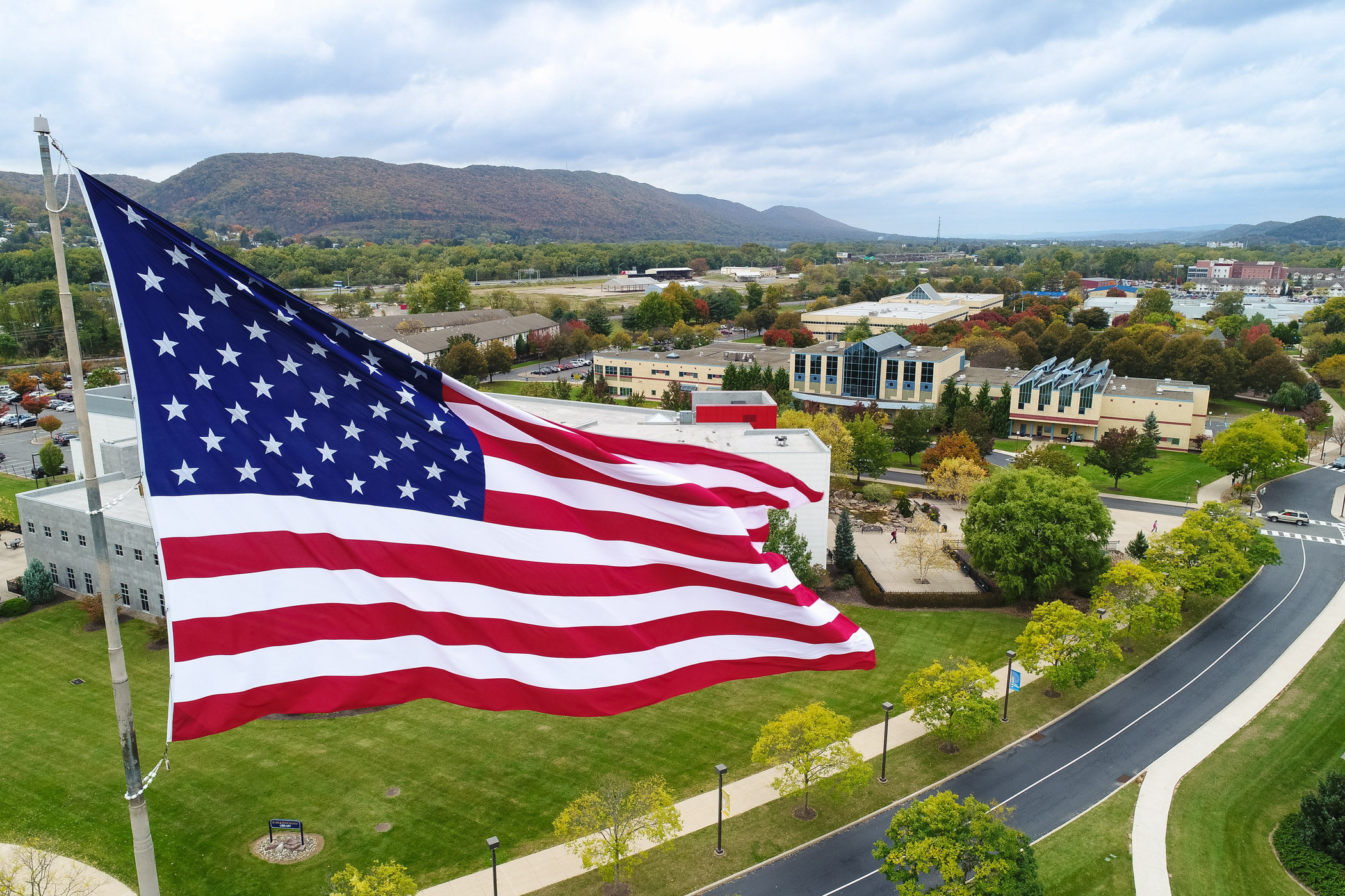 The United States flag flying with the Penn College campus behind it