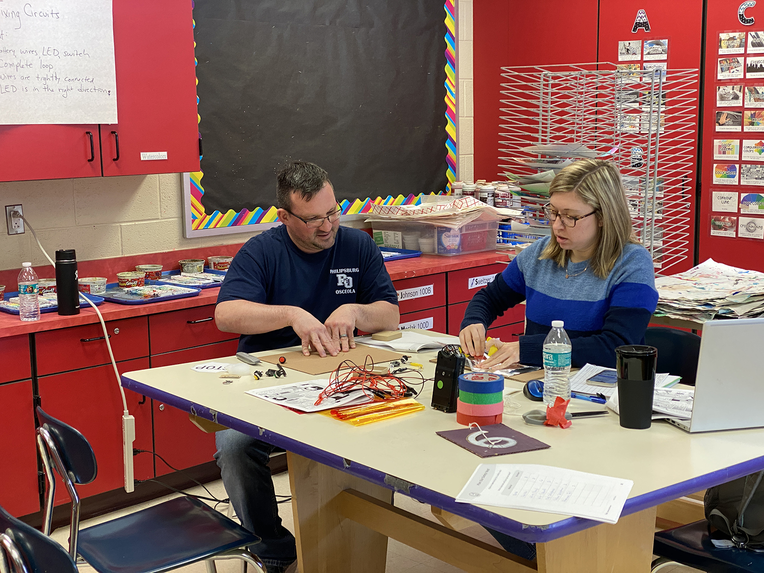 Two teachers sit at a table working on a project as part of their training.