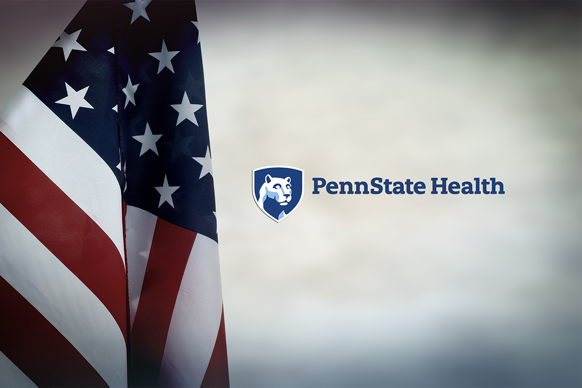 An American flag hangs down on the left, and to the right is the Penn State Health logo.