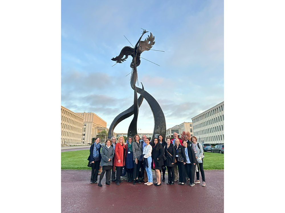 A large group of people posing for a picture in front of a sculpture in Normandy