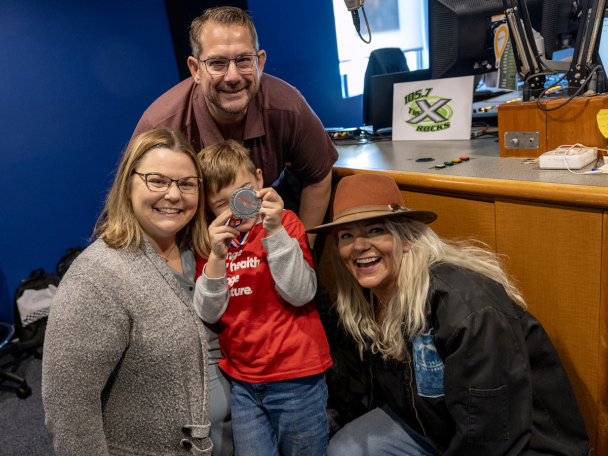 Three adults and one child pose for a photo in a radio studio, smiling.