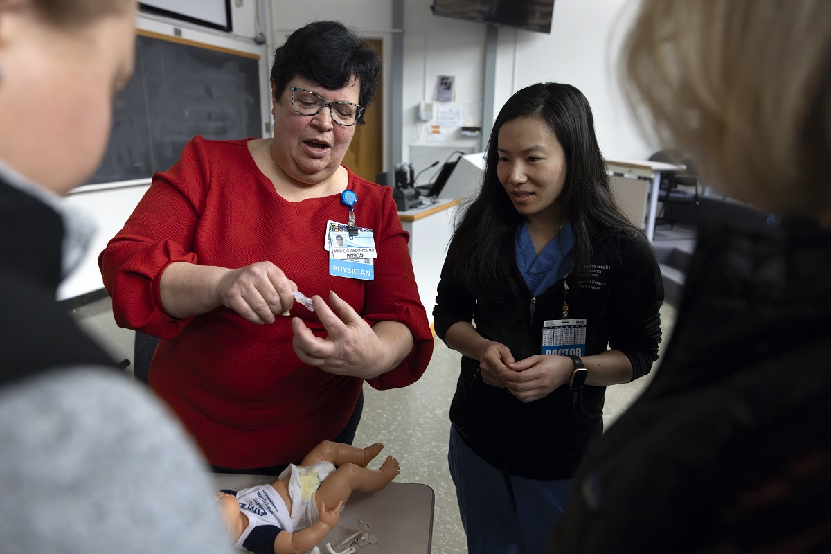 A woman on the left holds a feeding tube and teaches a group of surgical residents.