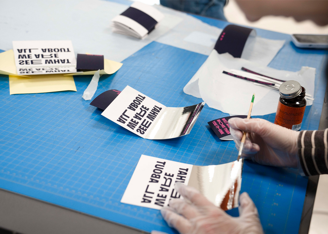 A blue drafting table with invitations atop that are being put together by hand.