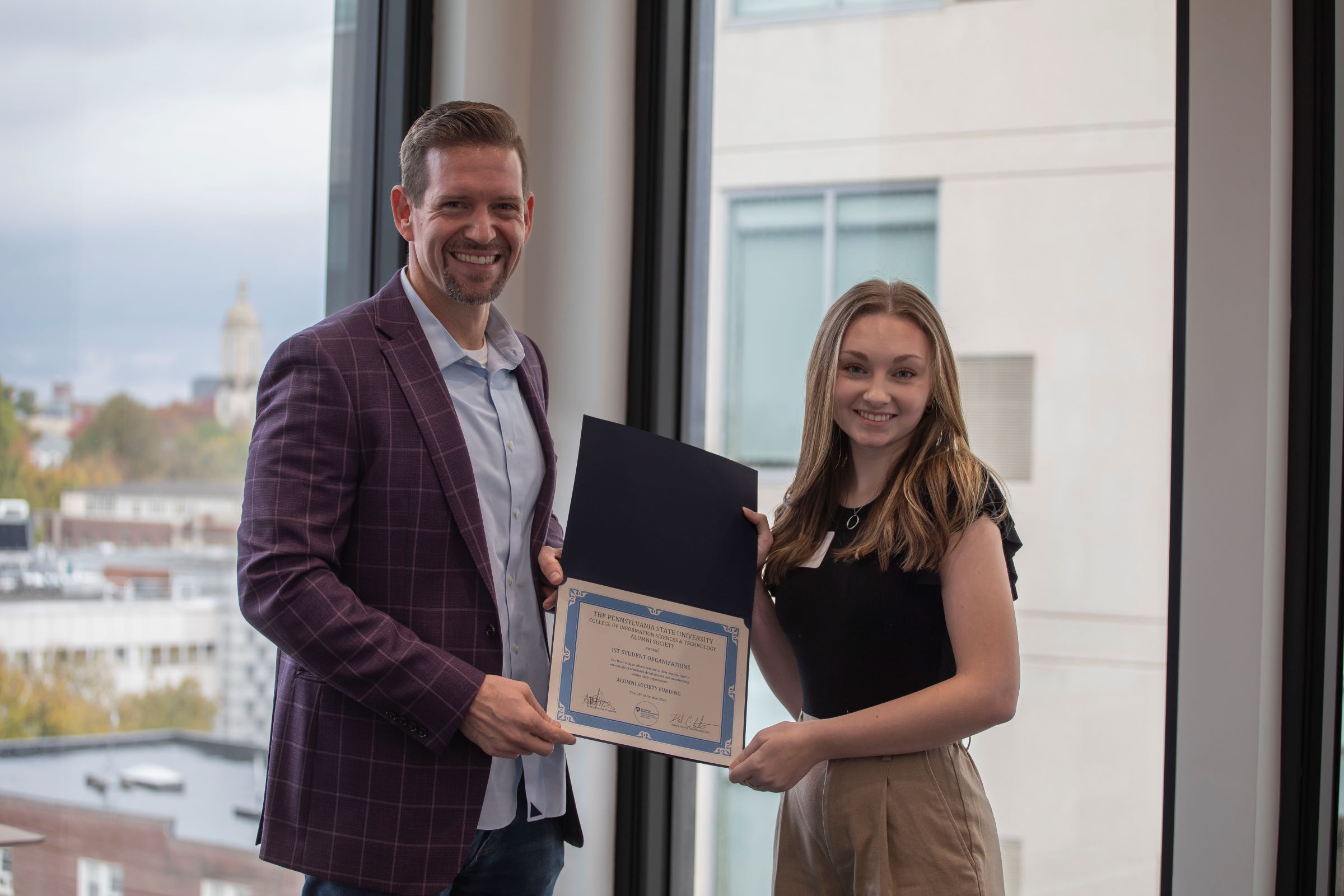 person in suit jacket and beard presents certificate to college student