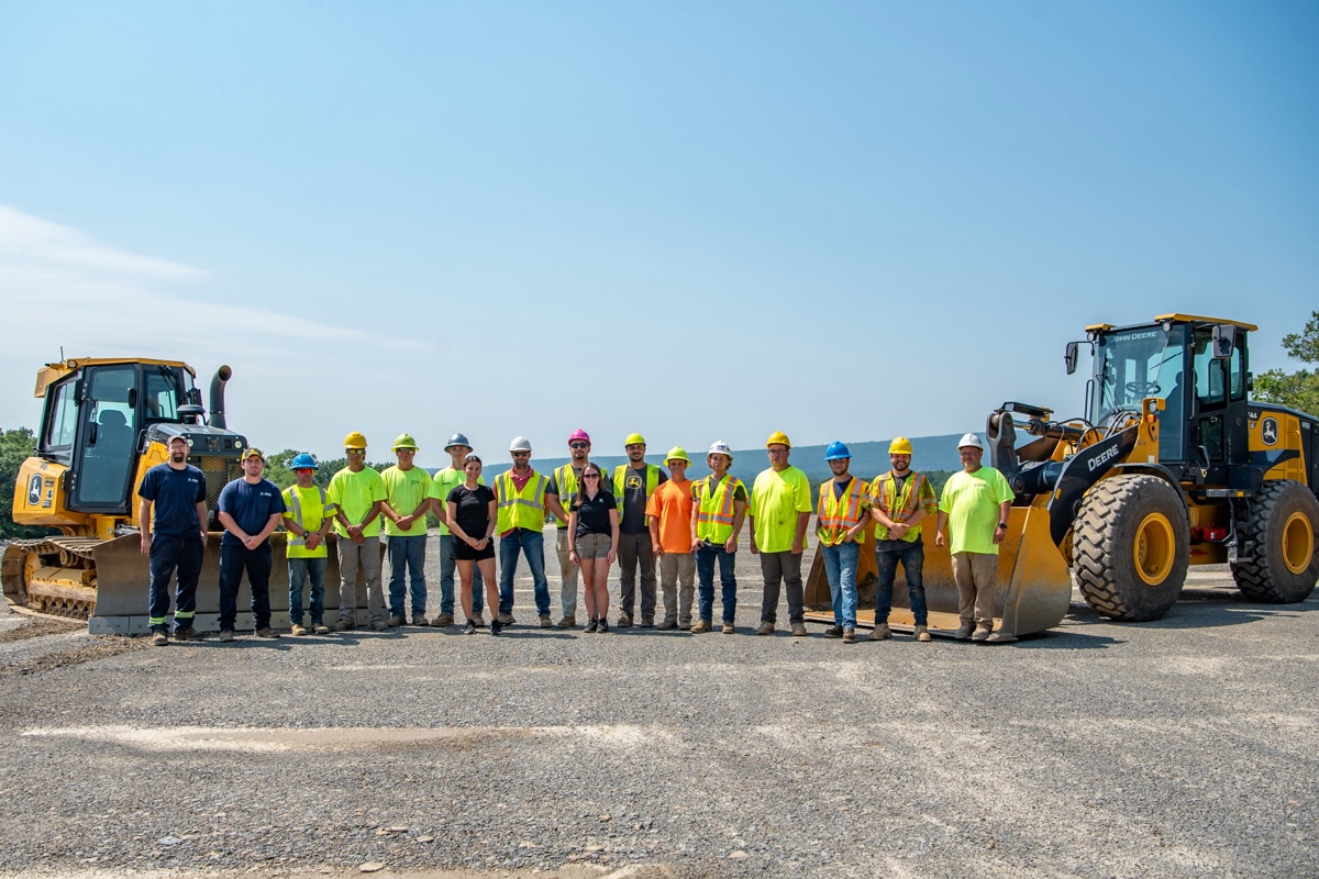 A group of people standing between two pieces of John Deere heavy equipment.