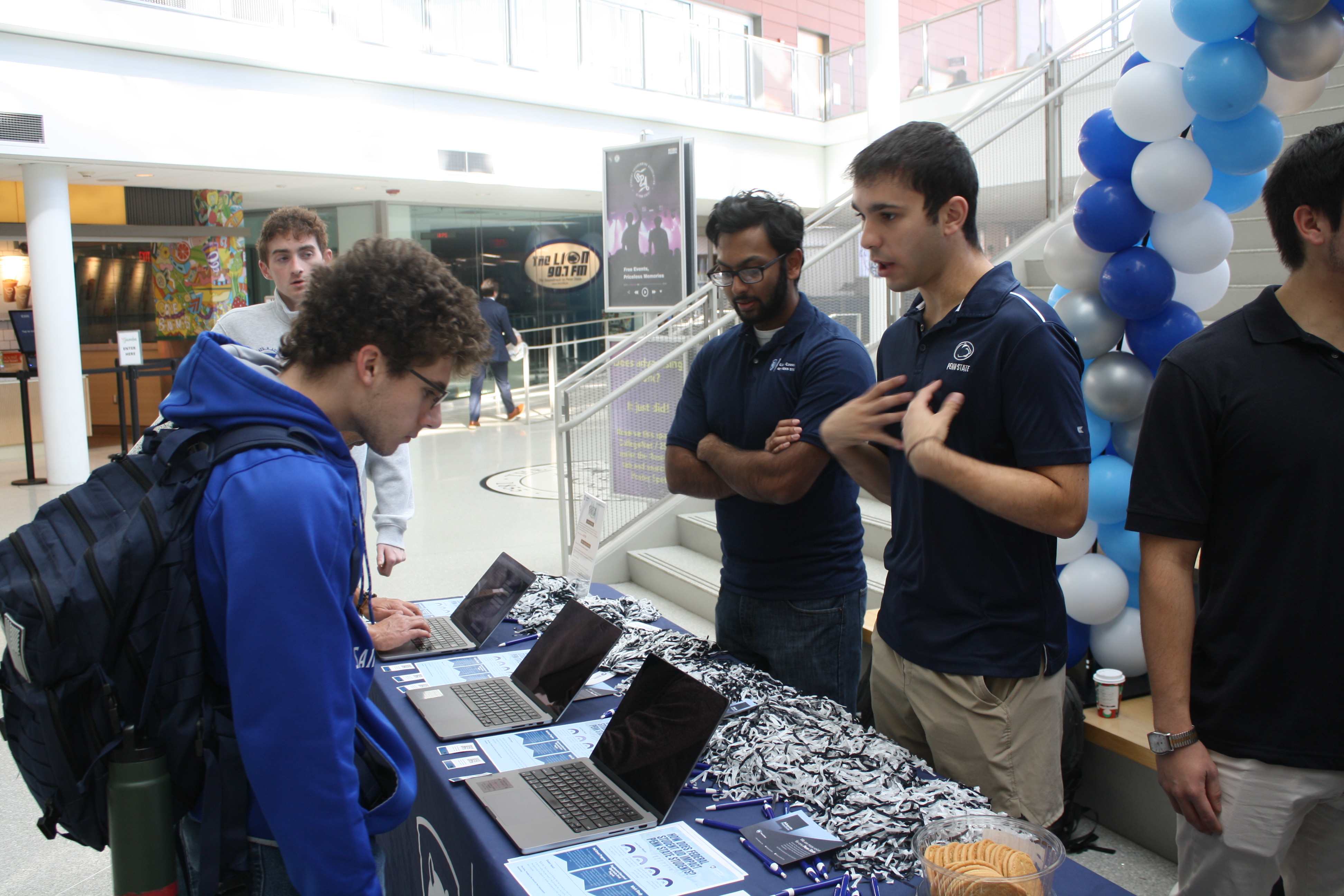 students standing behind a table talking with another student 