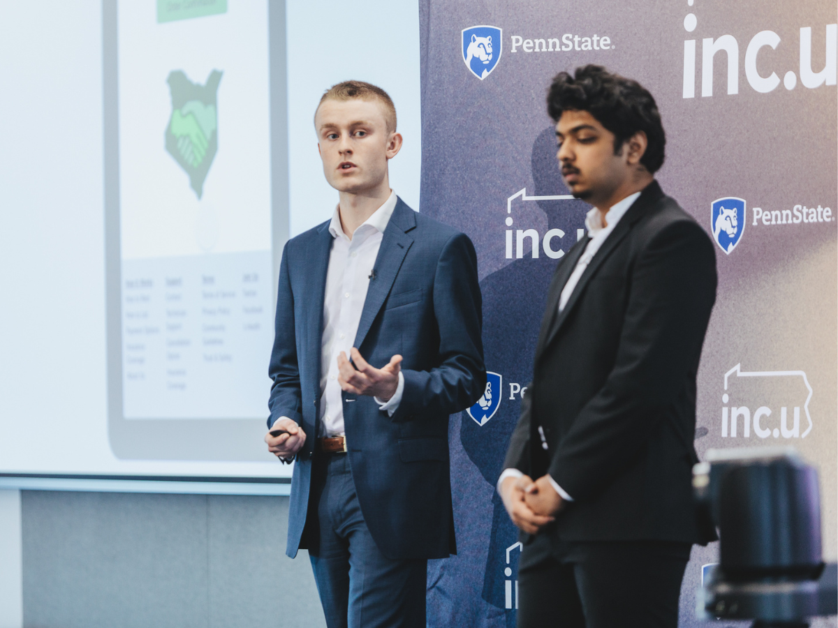 Two students pitching their startup in front of an Inc.U banner