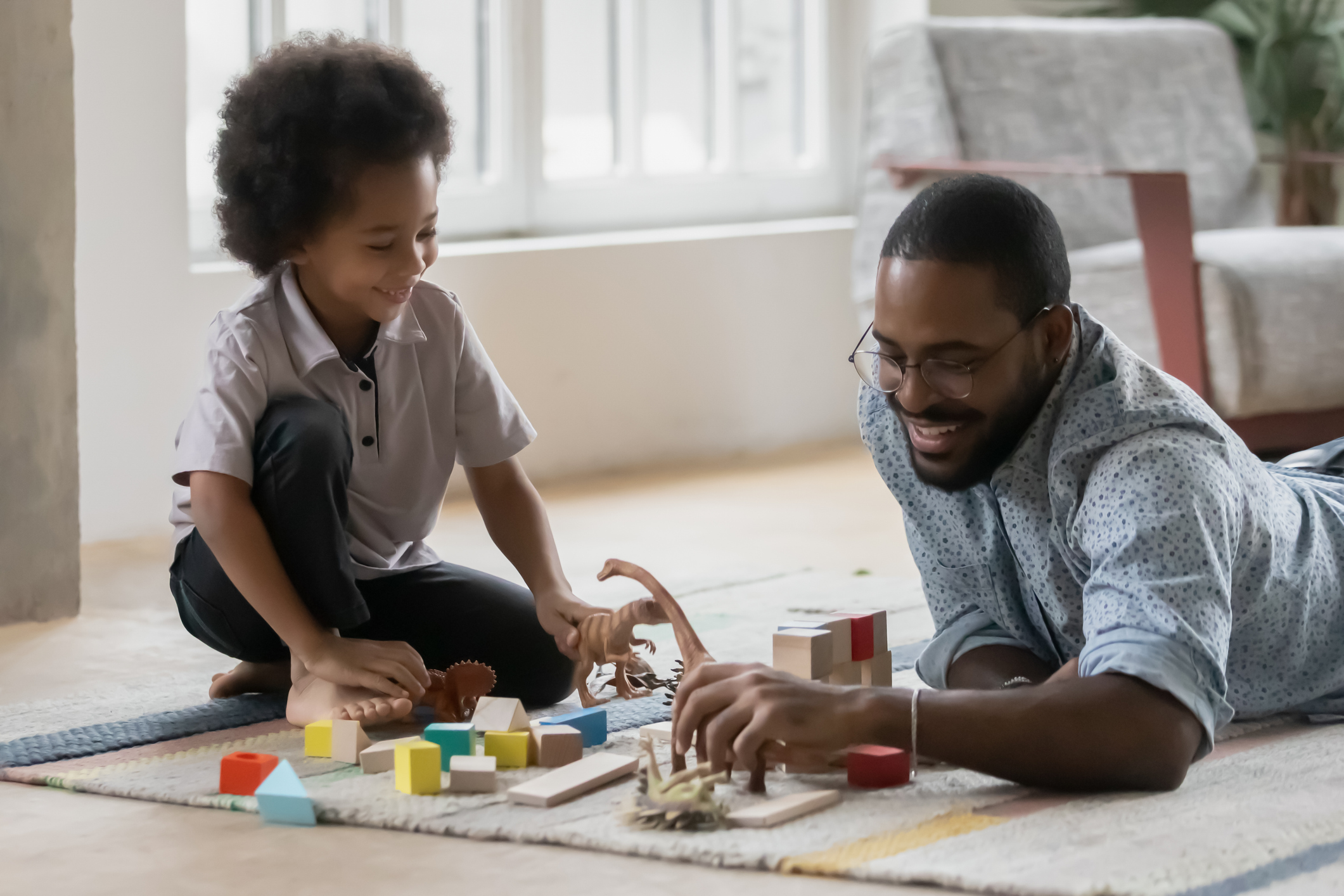 Family spend time together enjoy playtime in cozy living room, young caring father teach little kid play with son using wooden colorful block and dinosaur set toys on warm floor at modern home.