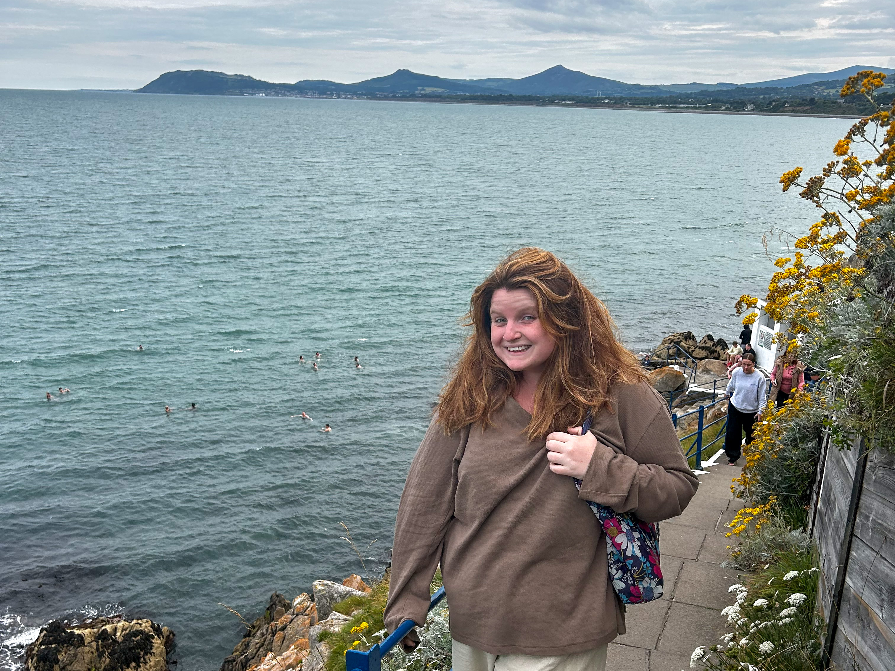 Teagan Mayr standing on a cliffside walking path overlooking the water.