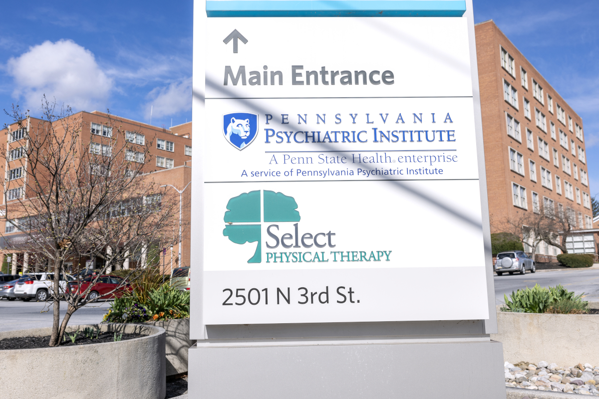 A brick, six-floor hospital is in the background. A sign in the foreground includes the logos for Pennsylvania Psychiatric Institute and Select Physical Therapy.