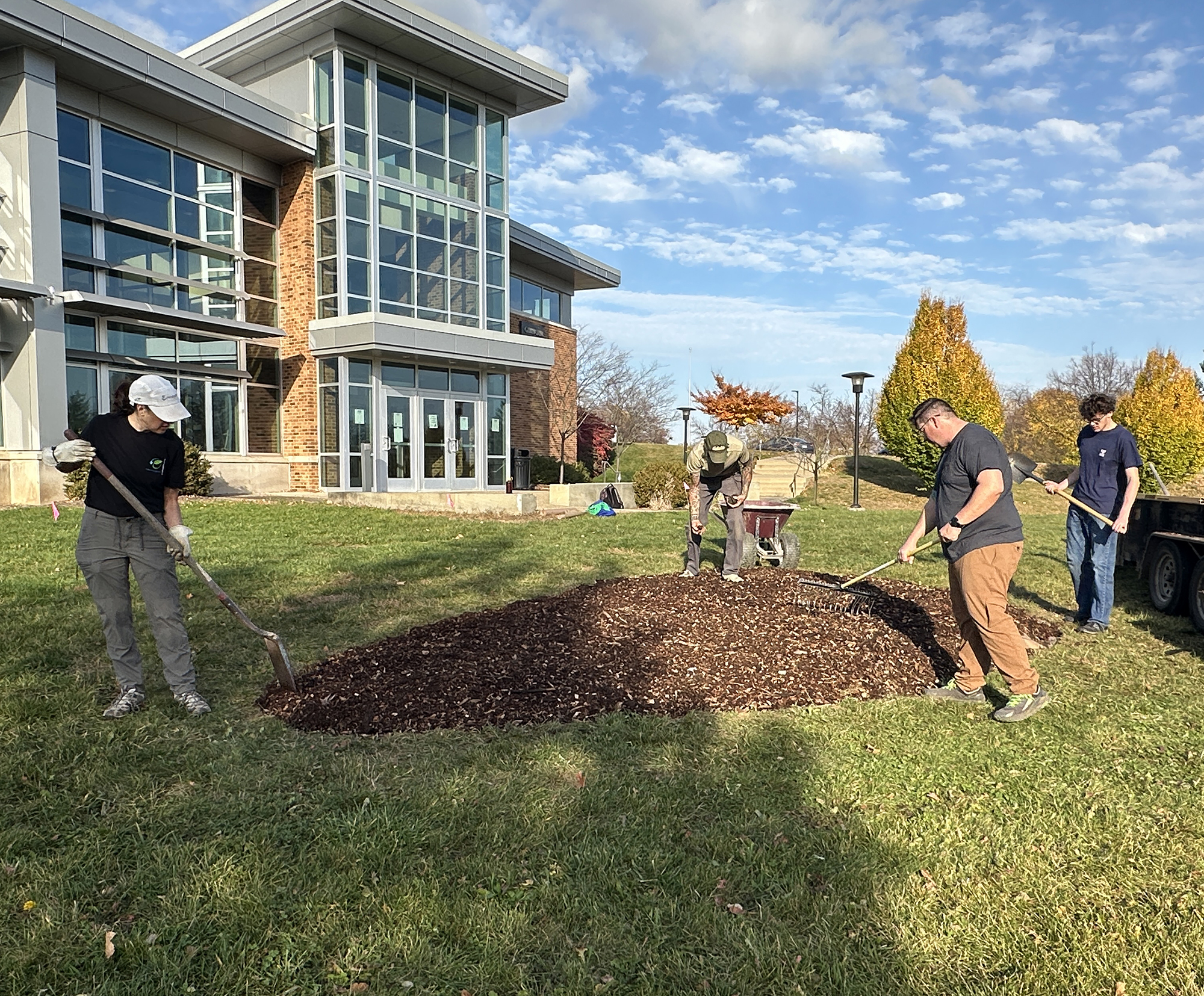 Four people work with shovels and rakes to prepare an area of mulch.