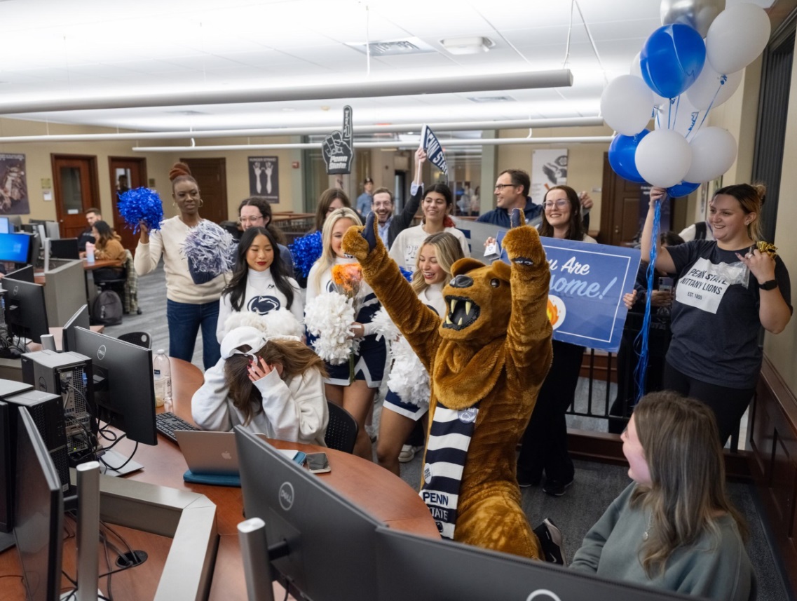 The Nittany Lion and a crowd of Penn Staters surprise a student at a computer