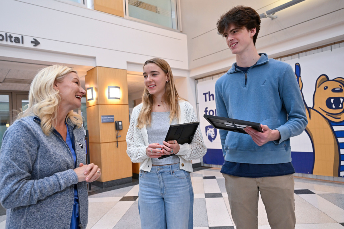 A female nurse speaks to a female and male high school student. The students are holding awards for performing life-saving actions. 