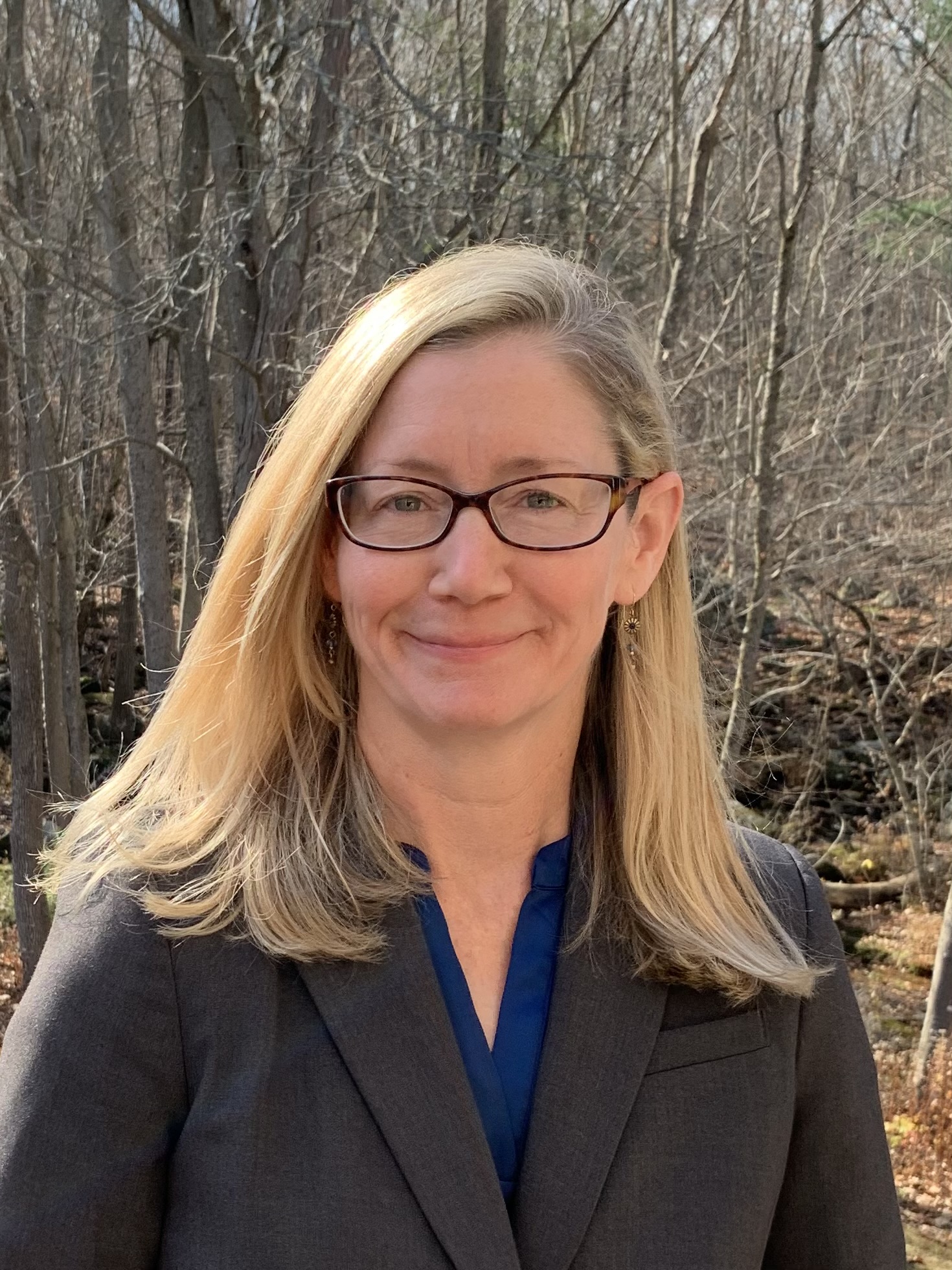 A blonde woman with glasses looks at the camera with a smile.