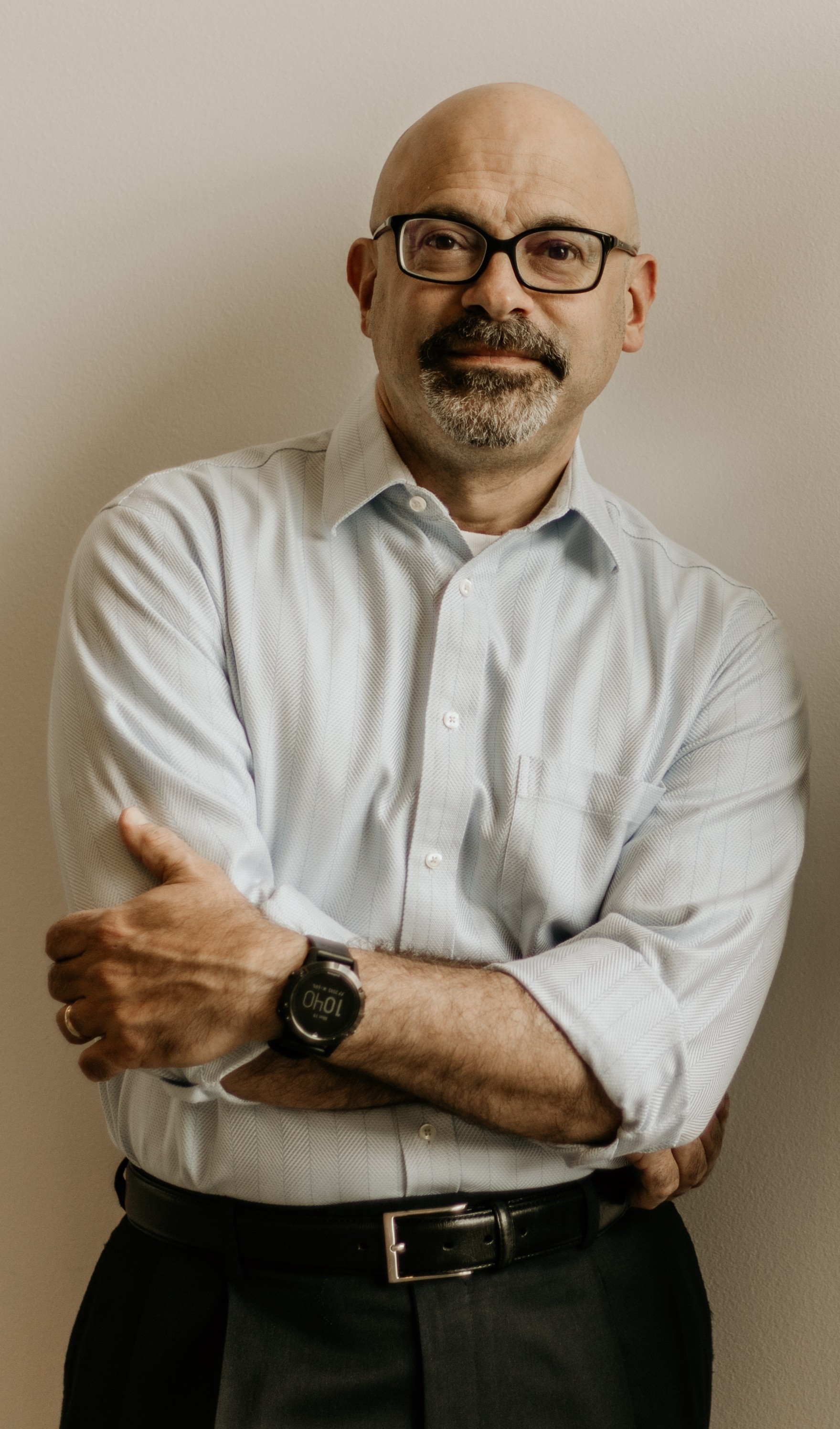 Image of a white man with a bald head wearing black framed glasses with his arms casually crossed.