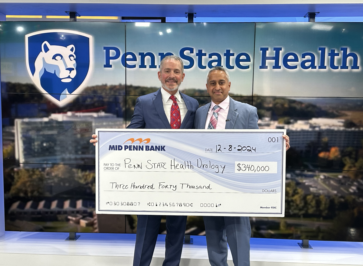 Two men in suits pose with a check made out to “Penn State Health Urology” in the amount of $340,000. A large Penn State Health logo is in the background.