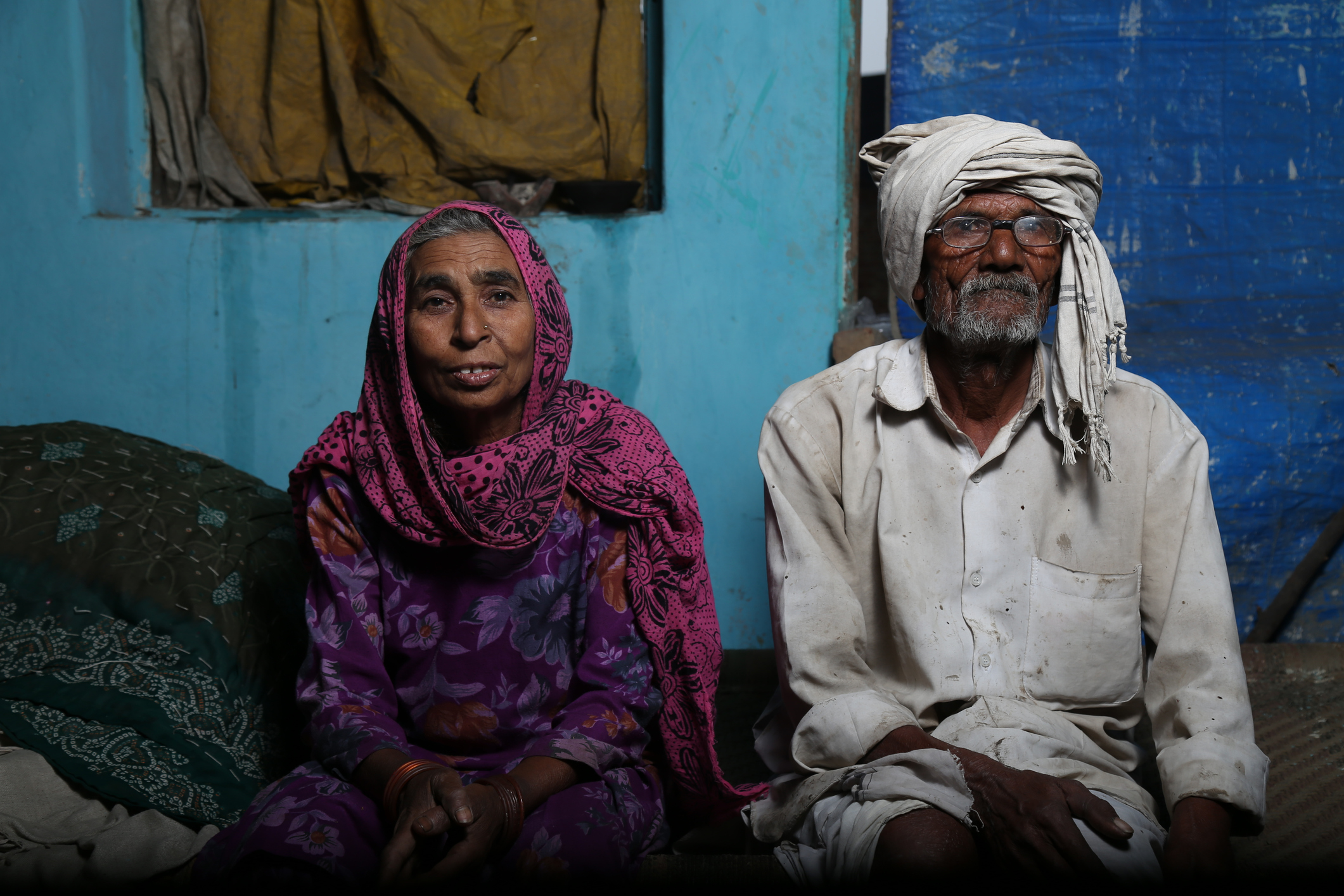 Older person with scarf on head and older person with head covering sit in their modest home