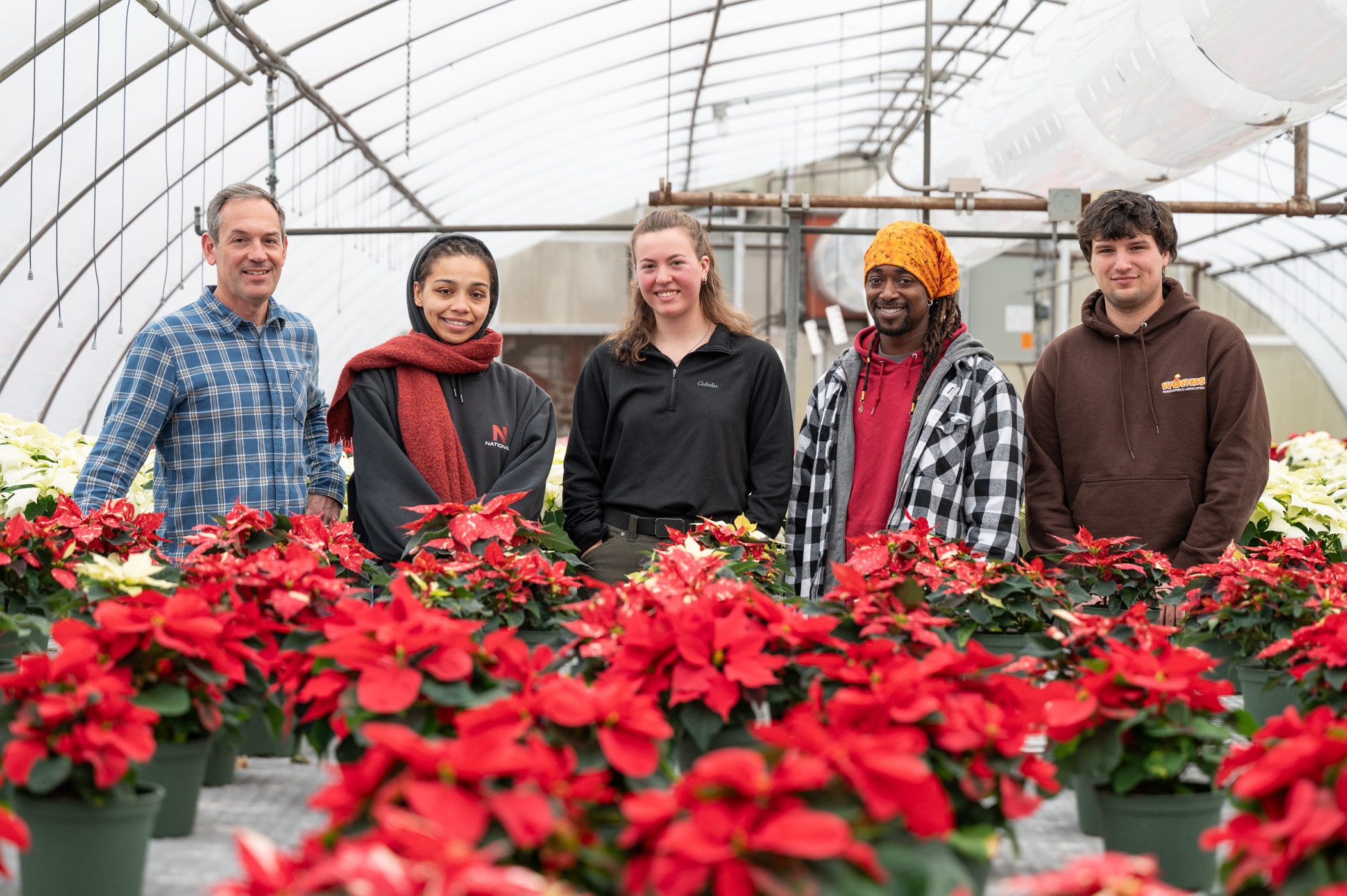 Five individuals gather around red flowers in a Penn College greenhouse.