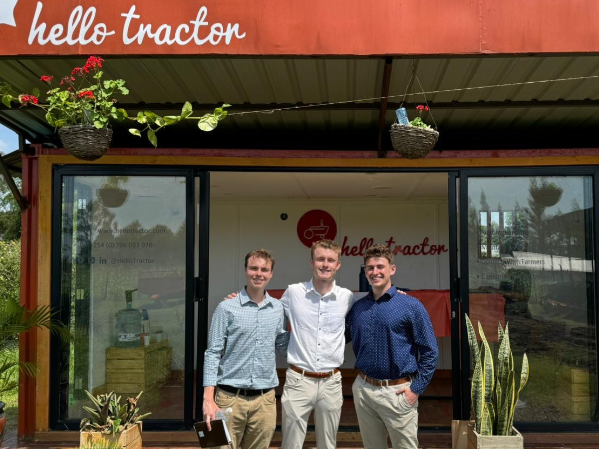 Three individuals pose for photo in front of building with sign that reads Hello Tractor