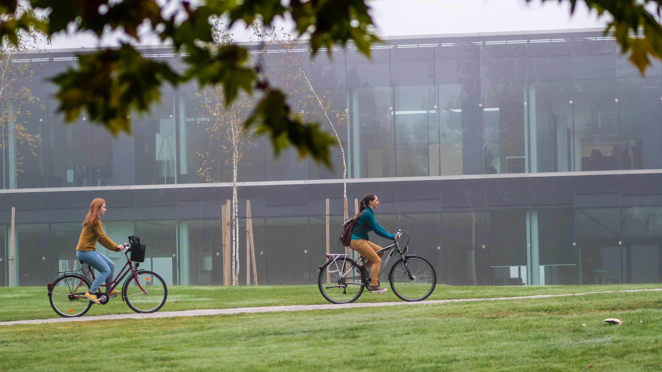 two women bicycling in front of a university building