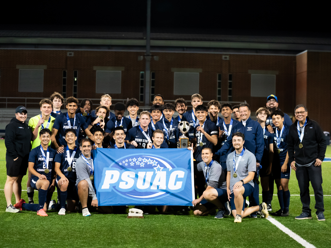 male soccer players pose for a group photo on a soccer field with a blue flag