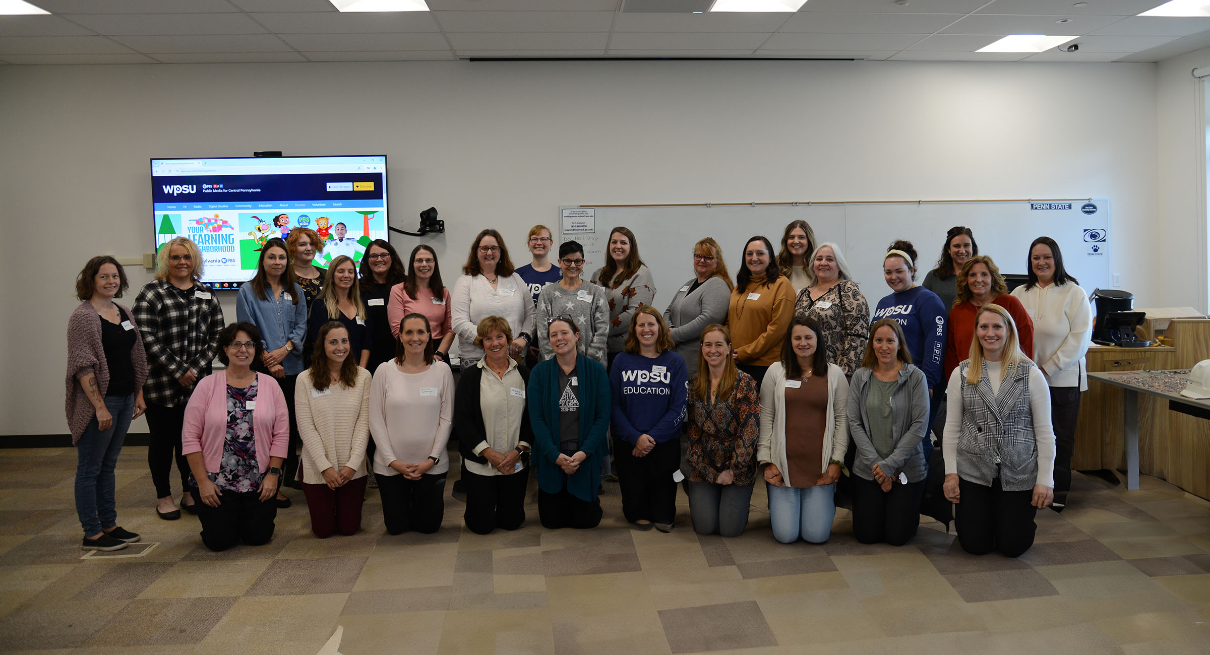 Photo of people standing in two rows in front of a presentation screen.