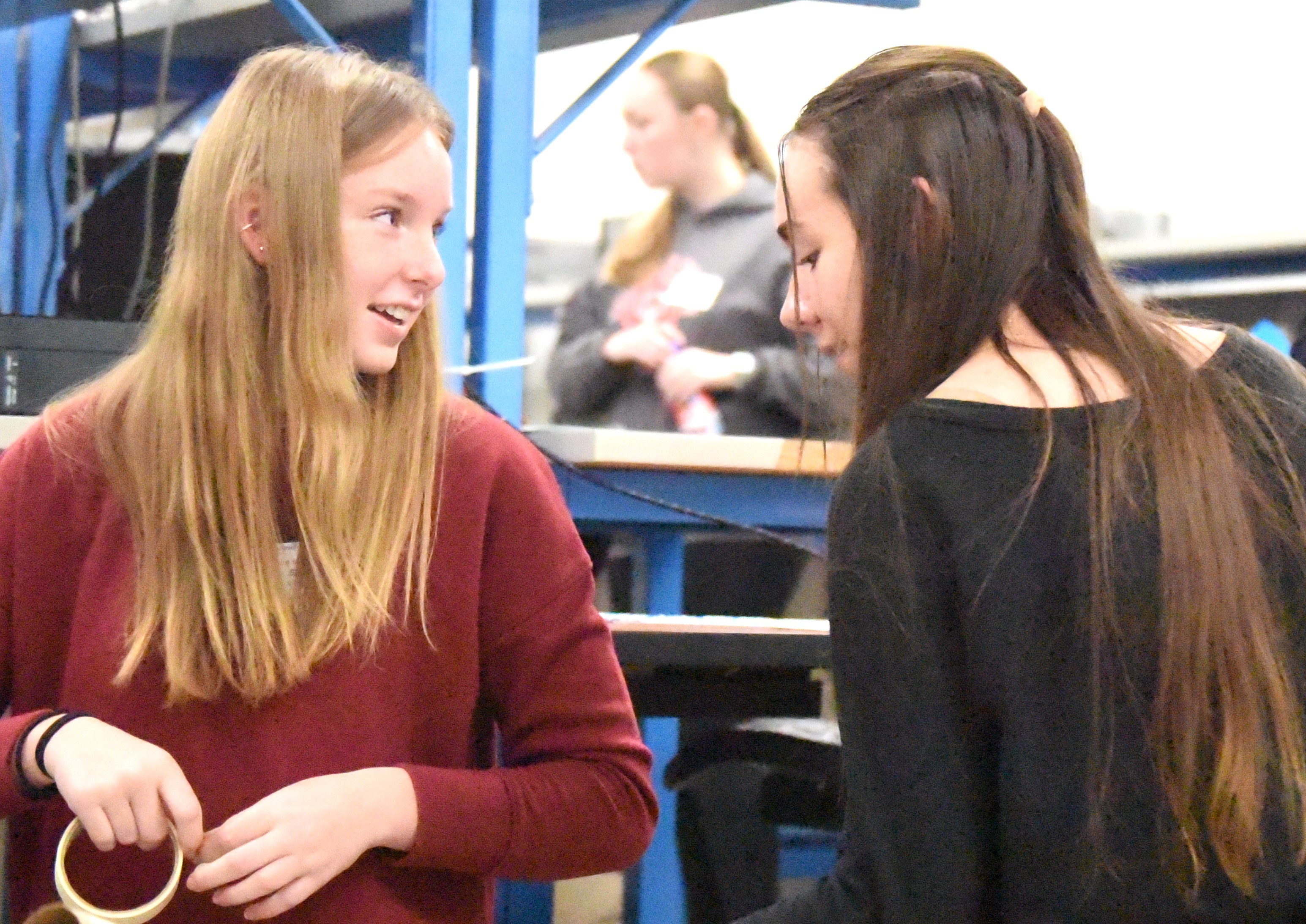 Two high school girls face each other and smile while building a model pipeline out of cardboard tubes.