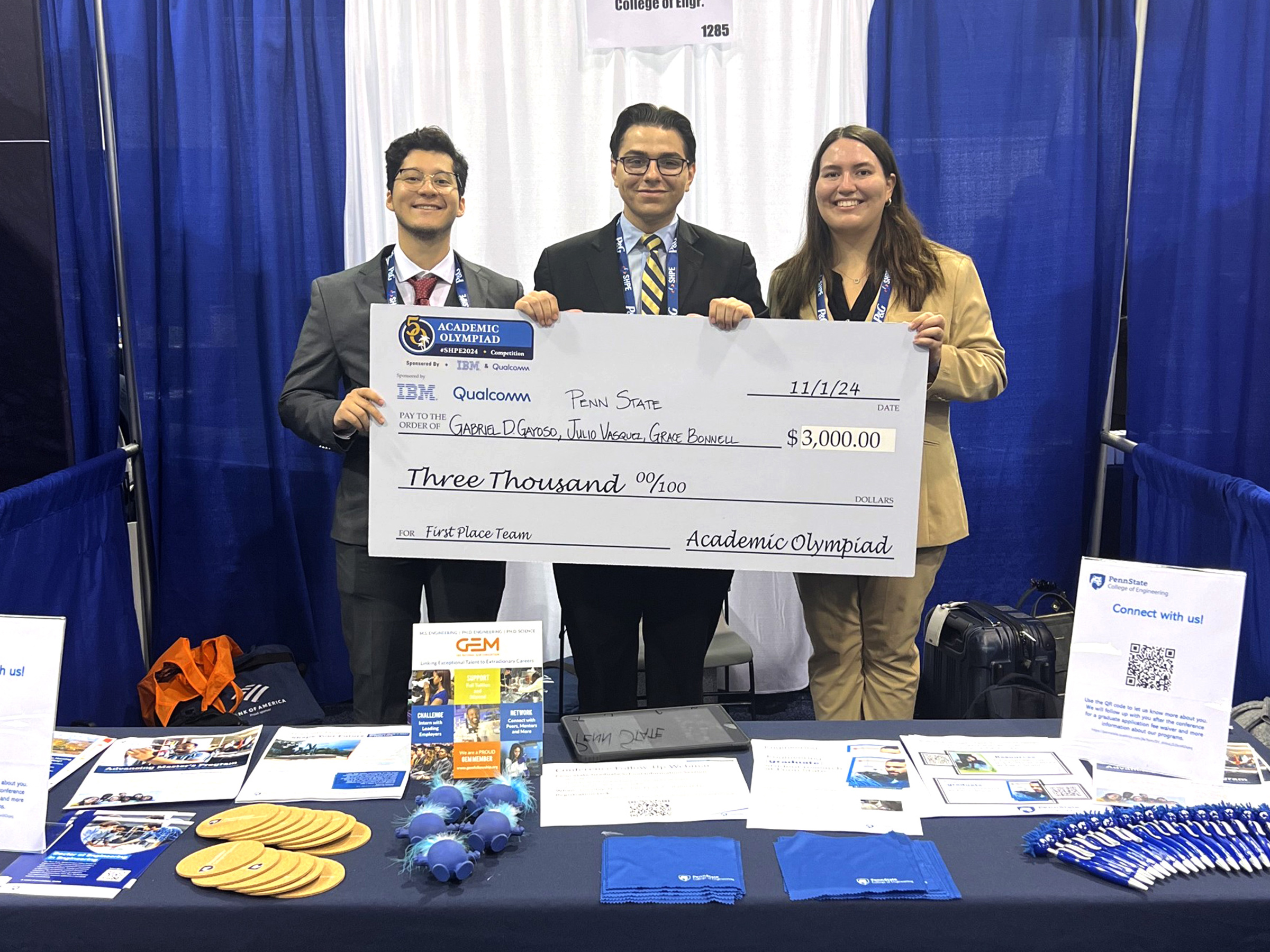 Three individuals hold a large check at a conference booth.