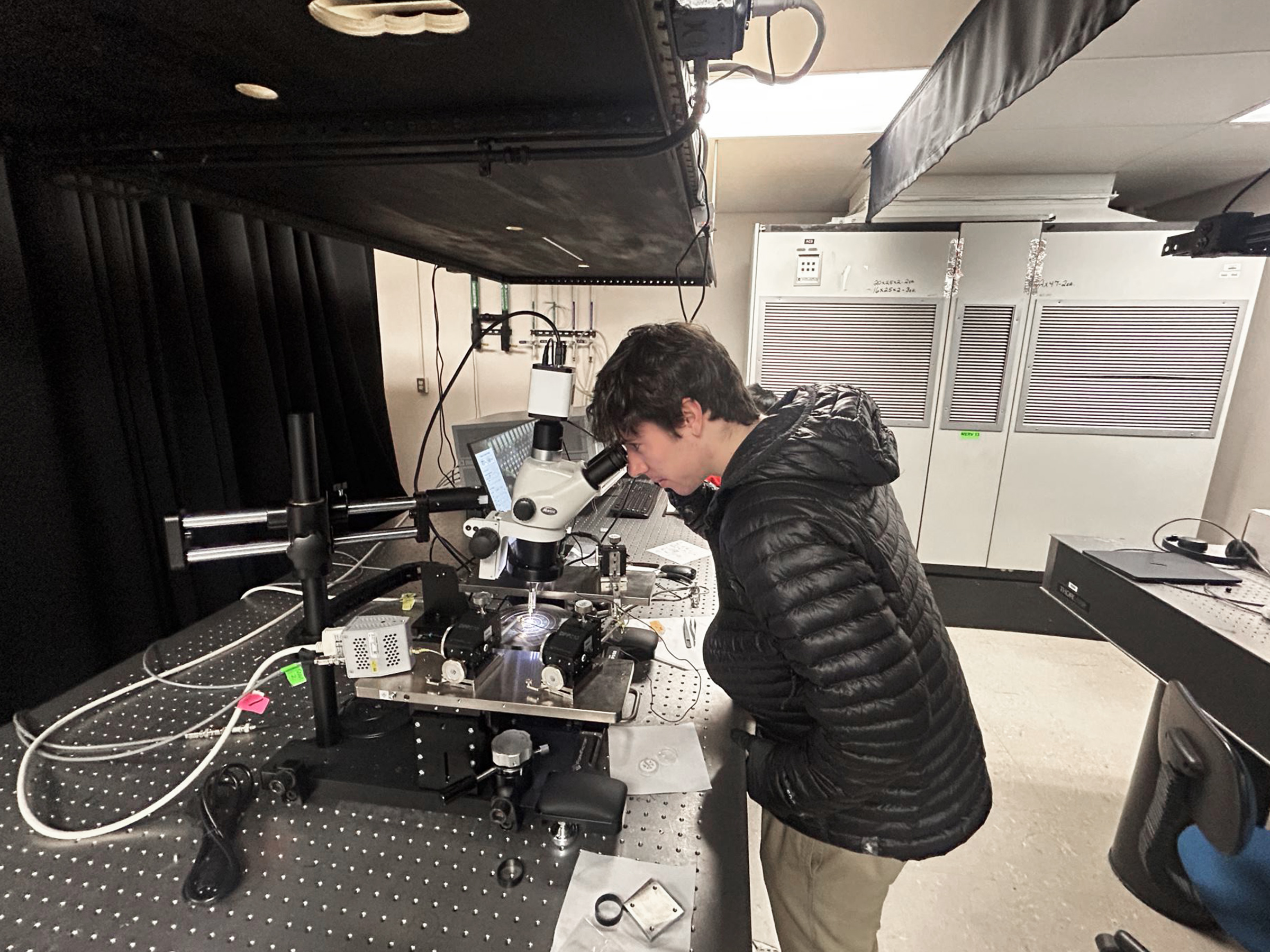 Person standing in a lab looking through a microscope at a machine