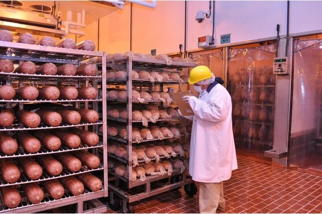 A person in a hard hat inspecting food stored on racks in a warehouse setting