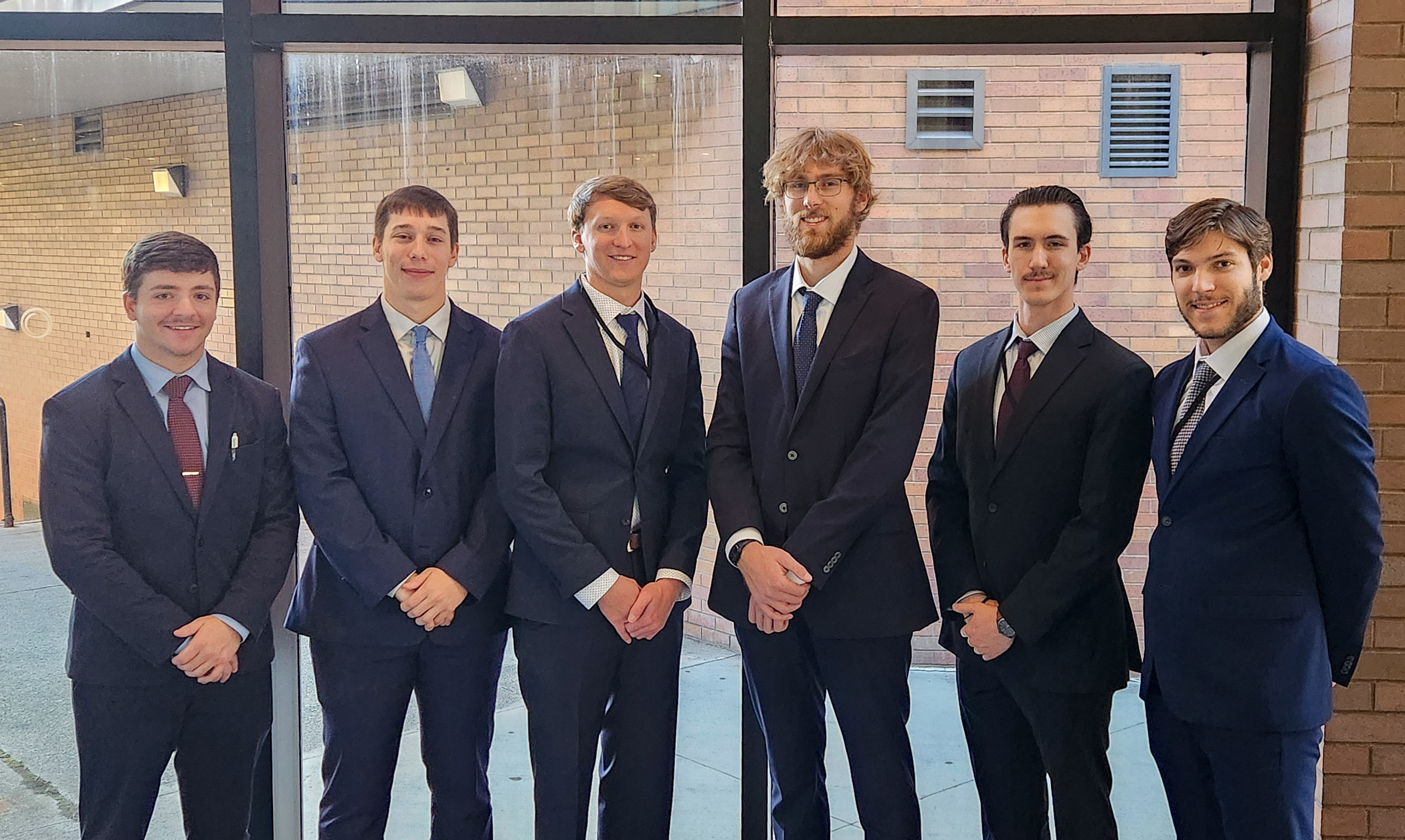 Six people in business suits stand together for a photo.