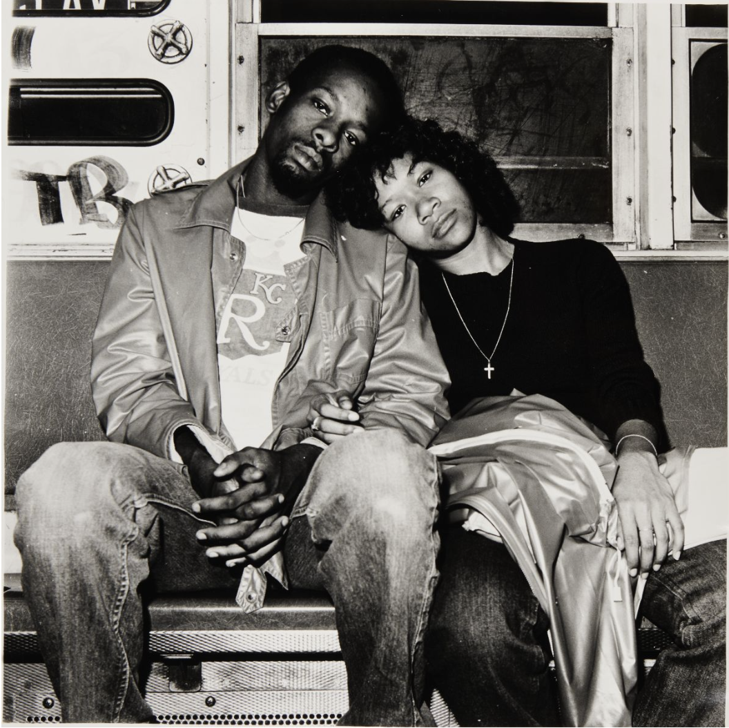 Photo of a seated Black couple leaning against each other on a subway train