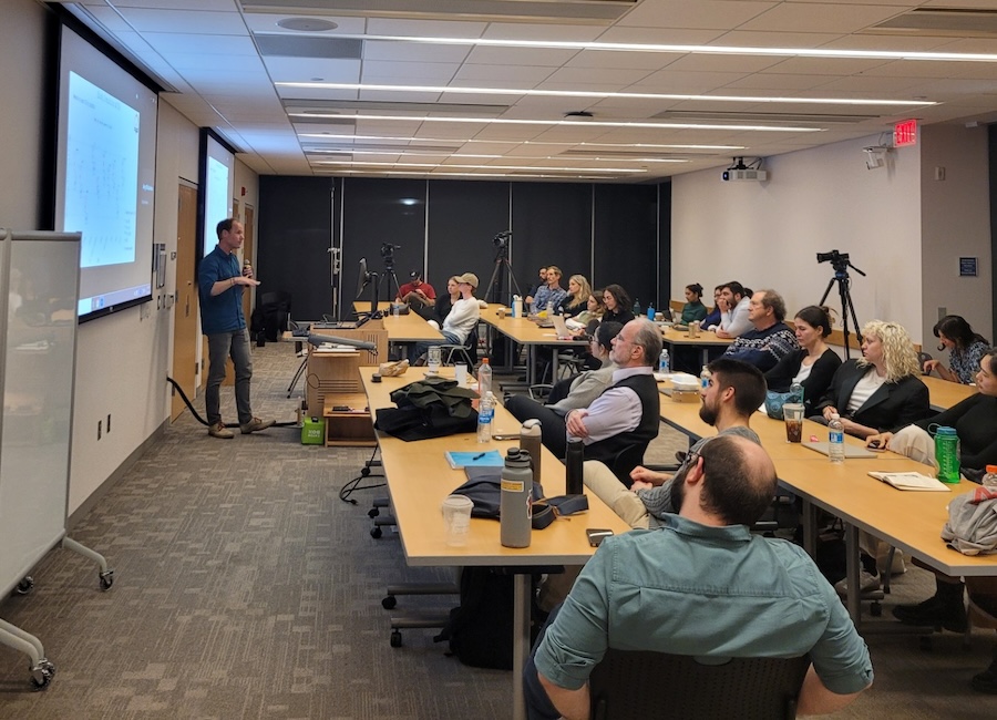  2024 Consortium on Moral Decision-Making Conference image shows a presenter leading a talk in a small room full of people seated at tables.