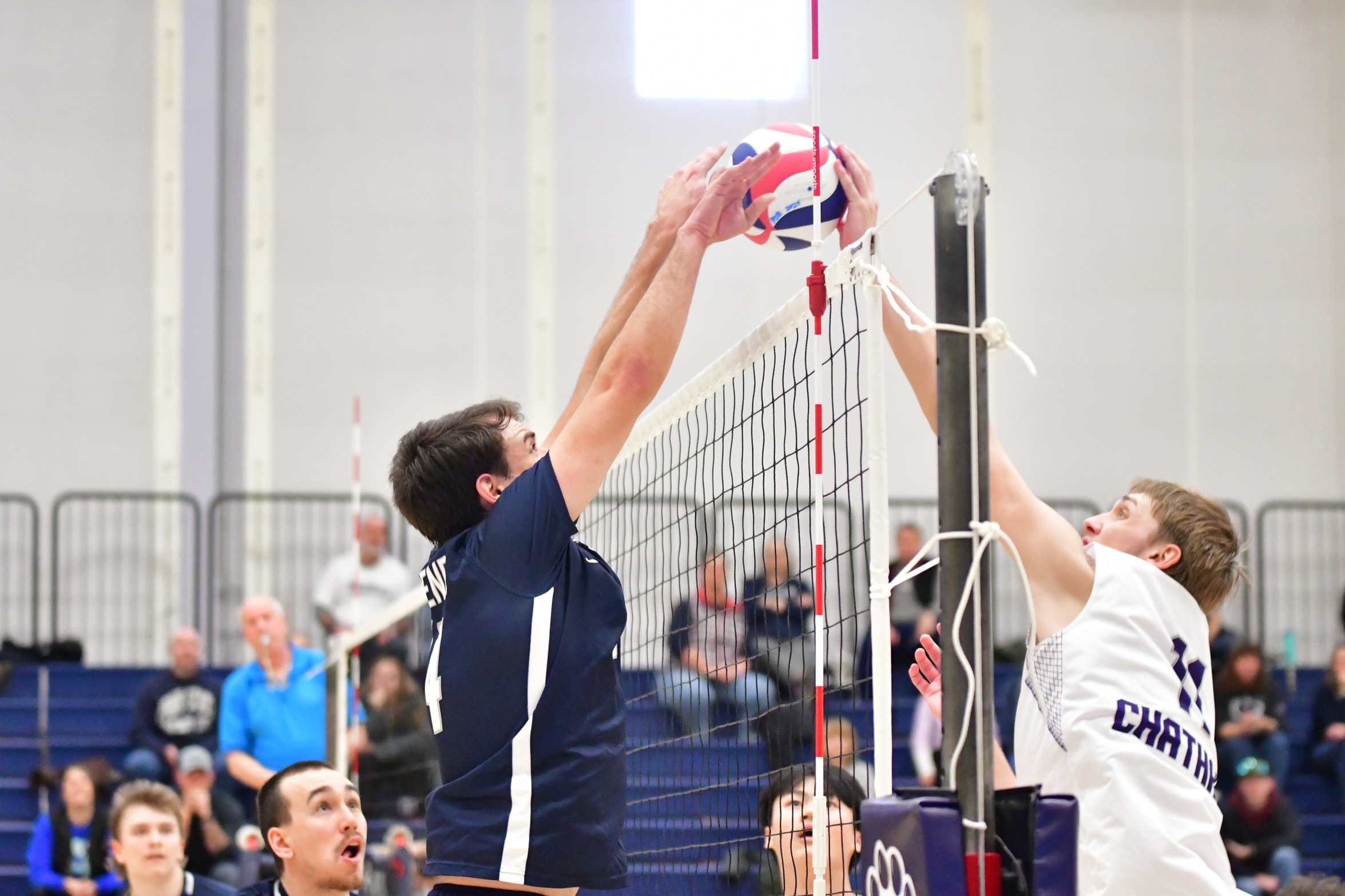 Two male volleyball players jump while facing each other at the net.