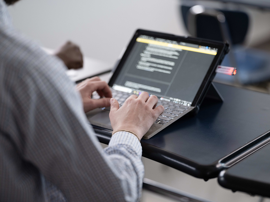 An image of the hands of someone who is seated and working on a laptop computer.