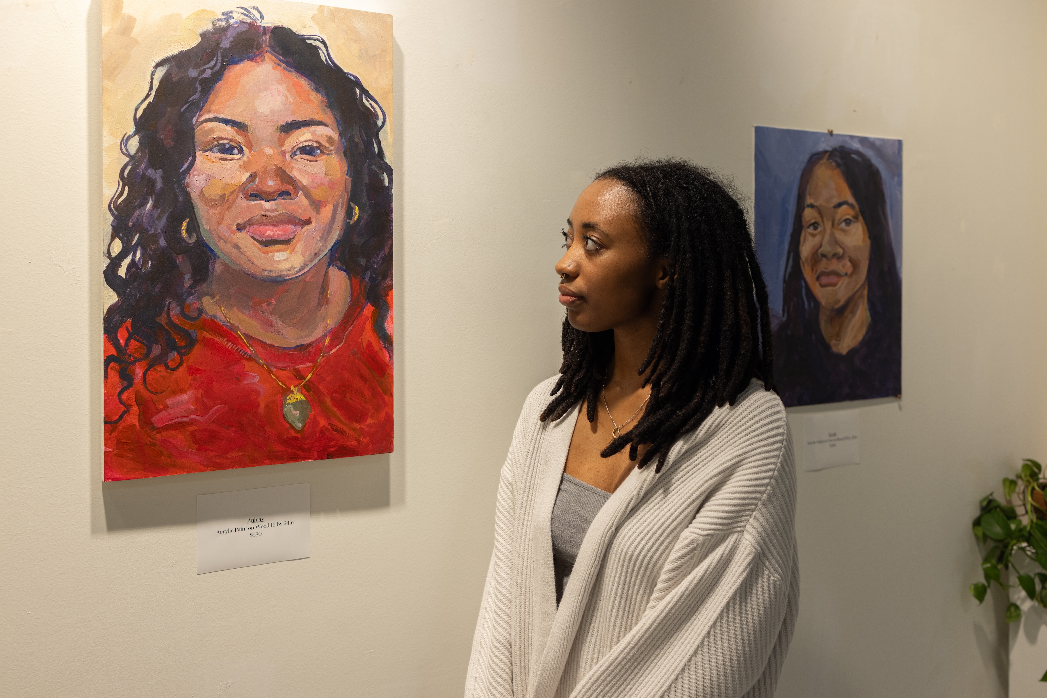 A young Black woman looks at a portrait on the wall.