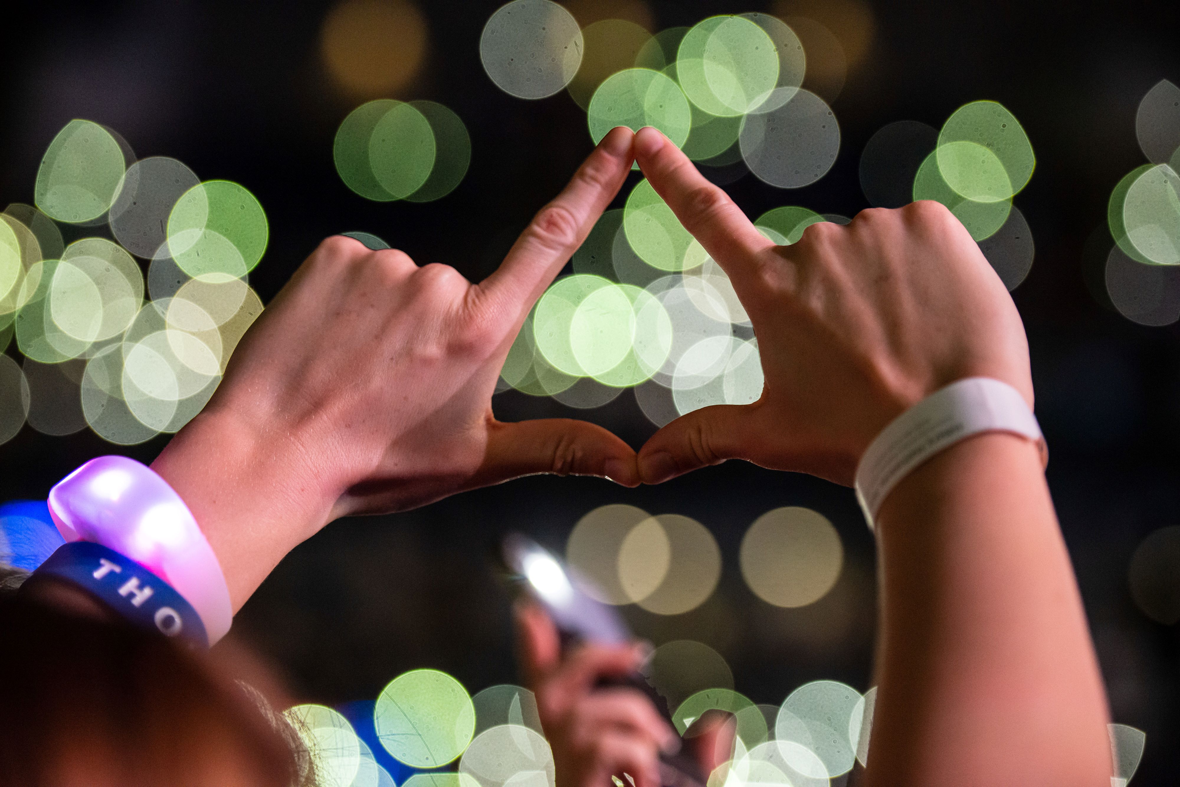two hands in the air coming together to make a diamonds shape infront of bright lights