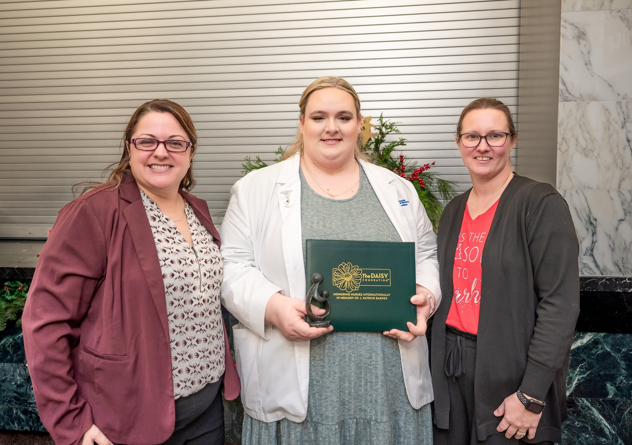 Three people stand in a row, one is holding an award certificate.